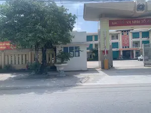 Bức ảnh chụp ban ngày lối vào một trụ sở cơ quan công quyền, có khả năng là trụ sở Công an huyện Vĩnh Lộc, tỉnh Thanh Hóa. Địa điểm này bao gồm một tòa nhà chính nhiều tầng ở phía sau, một cổng vào lớn có mái che, và một chốt gác nhỏ màu trắng ở bên trái. Trên vòm cổng có gắn Quốc huy Việt Nam và dòng chữ vàng "BẢO VỆ AN NINH TỔ QUỐC". Một thanh chắn barie tự động màu vàng đang hạ xuống ở lối vào. Bên trong sân có một chiếc ô tô màu trắng đang đỗ. Khung cảnh được trang trí bằng nhiều băng rôn, cho thấy bối cảnh có thể là vào dịp Tết Nguyên Đán. Không có hoạt động nào của con người được ghi lại. Các văn bản có thể nhận dạng bao gồm:。- Trên vòm cổng: "BẢO VỆ AN NINH TỔ QUỐC".。- Băng rôn đỏ trên tòa nhà: "Chúc Mừng Năm Mới Xuân Giáp Thìn 2024".。- Băng rôn phía trên lối vào tòa nhà: "XÂY DỰNG LỰC LƯỢNG CAND THẬT SỰ TRONG SẠCH, VỮNG MẠNH, CHÍNH QUY, TINH NHUỆ, HIỆN ĐẠI".。- Băng rôn dọc trên cột cổng: "LỰC LƯỢNG CÔNG AN VĨNH LỘC LÀ CHẮN PHÒNG CHỐNG DỊCH COVID-19...".。- Băng rôn đỏ bên trái, bị cây che khuất một phần: "... KẾT QUẢ LẬP THÀNH TÍCH ... THÌN 2024".。- Biển báo nhỏ trên thanh chắn barie: "XUẤT TRÌNH GIẤY TỜ" (chữ khó đọc nhưng có thể suy đoán).。（日本語訳）。日中に撮影された、ある政府機関の庁舎の入り口の写真。タインホア省ヴィンロック県警察署である可能性が高い。この場所は、後方にある多層階の本館、屋根付きの大きな門、そして左側にある小さな白い警備員詰所で構成されている。入り口では、黄色い自動遮断機が下りている。敷地内には白い車が一台駐車している。風景は多くの横断幕で飾られており、テト（旧正月）の時期であることがうかがえる。人の活動は記録されていない。識別可能なテキストは以下の通り：。- 門のアーチ上：「BẢO VỆ AN NINH TỔ QUỐC」（祖国の安全保障を守る）。- 建物上の赤い横断幕：「Chúc Mừng Năm Mới Xuân Giáp Thìn 2024」（2024年甲辰の新年あけましておめでとうございます）。- 建物入口の上の横断幕：「XÂY DỰNG LỰC LƯỢNG CAND THẬT SỰ TRONG SẠCH, VỮNG MẠNH, CHÍNH QUY, TINH NHUỆ, HIỆN ĐẠI」（真に清廉で、強固、正規、精鋭、近代的な人民公安部隊を建設する）。- 門柱の縦型横断幕：「LỰC LƯỢNG CÔNG AN VĨNH LỘC LÀ CHẮN PHÒNG CHỐNG DỊCH COVID-19...」（ヴィンロック公安部隊はCOVID-19防疫の盾である...）。- 左側の赤い横断幕、木で一部が隠れている：「... KẾT QUẢ LẬP THÀNH TÍCH ... THÌN 2024」（... 功績を立てた結果 ... 辰 2024）。- 遮断機上の小さな標識：「XUẤT TRÌNH GIẤY TỜ」（書類を提示せよ）（文字は読みにくいが推測可能）。