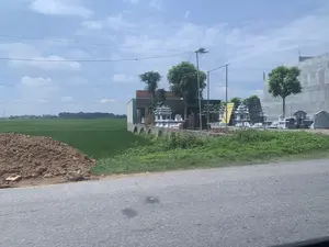 Bên trong hình ảnh có các biển quảng cáo với nội dung có thể đọc được là 'ĐÁ MỸ NGHỆ QUANG LINH' và 'HÓA TÁNG - ...'. Khung cảnh được chụp từ một con đường nhựa, nhìn về phía một cơ sở kinh doanh đá mỹ nghệ. Cơ sở này trưng bày rất nhiều sản phẩm lăng mộ, mộ bia và các công trình bằng đá khác để bán. Bên cạnh cơ sở là một cánh đồng lúa xanh rộng lớn. Ngoài ra còn có một đống đất ở ven đường, cây cối, cột đèn đường sử dụng năng lượng mặt trời, và một tòa nhà lớn bằng bê tông đang trong quá trình xây dựng. Bầu trời có mây và nhiều đường dây điện giăng ngang.。（日本語訳）。画像の中には、「ĐÁ MỸ NGHỆ QUANG LINH」と「HÓA TÁNG - ...」と読める内容の看板があります。風景はアスファルトの道路から撮影されており、美術石材を扱う事業所の方を向いています。この事業所は、販売用に多くの陵墓、墓石、その他の石造りの製品を展示しています。事業所の隣には、広大な緑の田んぼが広がっています。その他にも、道端に土の山、木々、太陽光発電の街灯柱、そして建設中の大きなコンクリートの建物があります。空は曇っており、多くの電線が横切っています。