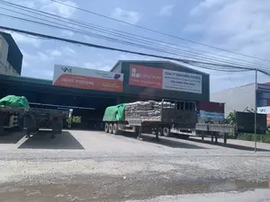 Bối cảnh là một kho hoặc đại lý vật liệu xây dựng của Công ty TNHH Hồng Phượng, tọa lạc tại huyện Vĩnh Lộc, tỉnh Thanh Hóa. Một chiếc xe tải lớn đang đỗ dưới mái che, trên thùng xe chất đầy các bao xi măng. Các xe tải và rơ-moóc khác cũng đang đỗ trong sân sỏi. Hoạt động chính là bốc xếp và chuẩn bị vận chuyển vật liệu xây dựng. Trên tòa nhà có nhiều biển hiệu quảng cáo với nội dung được ghi lại như sau:。Biển hiệu thứ nhất (màu cam và trắng):。- Logo: VAS Steel。- Tên công ty: CÔNG TY TNHH HỒNG PHƯỢNG。- Địa chỉ: Ninh Khang - Vĩnh Lộc - Thanh Hóa。- Khẩu hiệu: VỮNG VÀNG TÂM THÉP。- Ngành nghề: CHUYÊN KINH DOANH: XI MĂNG, SẮT THÉP。- Số điện thoại: 0963.672.453 - 0915.994.585。Biển hiệu thứ hai (màu xanh và trắng):。- Logo: LONG SON CEMENT。- Nội dung: XI MĂNG - CÔNG NGHỆ NHẬT BẢN。- Tên công ty và vai trò: CÔNG TY TNHH HỒNG PHƯỢỢNG, NHÀ PHÂN PHỐI XI MĂNG LONG SƠN, CỬA HÀNG VĨNH NINH。- Số điện thoại: 0963.972.453 - 0915.994.585。- Địa chỉ: XÃ VĨNH NINH, HUYỆN VĨNH LỘC, TỈNH THANH HOÁ。Biển hiệu thứ ba (nhỏ hơn, bị che một phần):。- Tên công ty: CÔNG TY HỒNG PHƯỢNG。- Nội dung: PHÒNG GIAO DỊCH BÁN HÀNG。（日本語訳）。背景は、タインホア省ヴィンロック県にあるホンフオン有限会社の建材倉庫または代理店です。大きなトラックが屋根の下に駐車しており、荷台にはセメント袋が満載されています。他のトラックやトレーラーも砂利の庭に駐車しています。主な活動は、建材の積み下ろしと輸送準備です。建物には多くの広告看板があり、その内容は以下の通りです。1番目の看板（オレンジと白）：。- ロゴ：VAS Steel。- 会社名：ホンフオン有限会社。- 住所：ニンカン - ヴィンロック - タインホア。- スローガン：鋼の心、揺るぎなく。- 業種：専門分野：セメント、鉄鋼。- 電話番号：0963.672.453 - 0915.994.585。2番目の看板（青と白）：。- ロゴ：LONG SON CEMENT。- 内容：セメント - 日本の技術。- 会社名と役割：ホンフオン有限会社、ロンソンセメント販売代理店、ヴィンニン店。- 電話番号：0963.972.453 - 0915.994.585。- 住所：タインホア省ヴィンロック県ヴィンニン社。3番目の看板（小さく、一部が隠れている）：。- 会社名：ホンフオン会社。- 内容：営業取引室