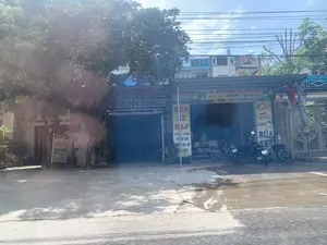 Bức ảnh chụp một con đường với nhiều cửa hàng nhỏ ven đường, đặc trưng cho một khu dân cư ở Việt Nam. Phía trước các cửa hàng có một vài chiếc xe máy đang đỗ. Một cây lớn ở bên trái che khuất một phần tầm nhìn. Phía trên là bầu trời xanh và hệ thống dây điện chằng chịt.。Nội dung các biển hiệu được ghi lại:。1. Biển hiệu bên trái (quán Hồng Quyên): "LÒNG LỢN", "CHÁO LÒNG". Đây là một quán ăn chuyên về các món từ lòng lợn.。2. Biển hiệu dọc ở giữa: "SỬA XE ĐẠP", "MUA - BÁN TRỨNG LỘN, TRỨNG GÀ, VỊT CÁC LOẠI". Đây là một cửa hàng vừa sửa xe đạp vừa bán các loại trứng.。3. Biển hiệu ngang ở giữa: "CUNG CẤP: NƯỚC MẮM THỊNH HƯƠNG", "MUA - BÁN: GẠO NẾP - GẠO TẺ, ĐẬU, LẠC - VỪNG - RAU CỦ QUẢ CÁC LOẠI". Đây là một cửa hàng tạp hóa bán các loại nông sản và thực phẩm.。4. Biển hiệu bên phải: "Cắt Tóc NAM", "RỬA XE". Đây là một tiệm cắt tóc nam kết hợp dịch vụ rửa xe.。Hoạt động chính được thể hiện qua các biển hiệu là kinh doanh buôn bán đa dạng các mặt hàng và dịch vụ tại gia, bao gồm bán đồ ăn, thực phẩm, sửa chữa và dịch vụ làm đẹp, vệ sinh xe cộ.。（日本語訳）。写真は、ベトナムの住宅街に特徴的な、道端に多くの小さな店が並ぶ通りを写したものです。店の前には数台のバイクが停まっています。左側にある大きな木が視界の一部を遮っています。上には青い空と、複雑に絡み合った電線があります。看板に書かれている内容は以下の通りです：。1. 左側の看板（ホン・クエン店）：「LÒNG LỢN（豚モツ）」、「CHÁO LÒNG（モツ粥）」。これは豚モツ料理を専門とする食堂です。2. 中央の縦長の看板：「SỬA XE ĐẠP（自転車修理）」、「MUA - BÁN TRỨNG LỘN, TRỨNG GÀ, VỊT CÁC LOẠI（ホビロン、鶏卵、アヒルの卵各種の売買）」。これは自転車修理と各種の卵の販売を兼ねた店です。3. 中央の横長の看板：「CUNG CẤP: NƯỚC MẮM THỊNH HƯƠNG（提供：ティンフーン・ヌクマム）」、「MUA - BÁN: GẠO NẾP - GẠO TẺ, ĐẬU, LẠC - VỪNG - RAU CỦ QUẢ CÁC LOẠI（売買：もち米 - うるち米、豆、落花生 - ごま - 各種野菜・果物）」。これは各種の農産物や食品を販売する雑貨店です。4. 右側の看板：「Cắt Tóc NAM（男性カット）」、「RỬA XE（洗車）」。これは男性向けの理髪店と洗車サービスを組み合わせた店です。看板に示されている主な活動は、自宅兼店舗での多様な商品やサービスの商売であり、飲食店、食料品販売、修理、美容サービス、車両清掃などが含まれます。