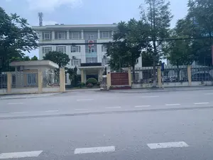 Bức ảnh chụp một tòa nhà văn phòng nhiều tầng, là một trụ sở cơ quan nhà nước, nhìn từ bên kia đường. Tại cổng vào có một tấm biển hiệu lớn màu đỏ ghi chữ màu vàng:。CỤC THUẾ TỈNH THANH HÓA。CHI CỤC THUẾ。KHU VỰC YÊN ĐỊNH - THIỆU HÓA。Dòng chữ nhỏ bên dưới ghi địa chỉ nhưng khó đọc.。Đây là trụ sở của Chi cục Thuế khu vực Yên Định - Thiệu Hóa, thuộc Cục Thuế tỉnh Thanh Hóa. Tòa nhà được sơn màu trắng, có nhiều cửa sổ. Trên mặt tiền tòa nhà có treo cờ Tổ quốc Việt Nam và cờ Đảng. Khuôn viên được bao quanh bởi hàng rào sắt, có một chốt bảo vệ ở cổng. Bên trong sân có thể thấy một số xe máy và ô tô đang đỗ. Xung quanh tòa nhà có nhiều cây xanh. Trên nóc nhà có một cột ăng ten viễn thông. Phía trước là một con đường nhựa với vạch kẻ đường đứt quãng. Quang cảnh vắng vẻ, không có hoạt động nào đáng chú ý đang diễn ra.。（日本語訳）。写真は、道路の向こう側から見た、ある政府機関の本庁舎である多層階のオフィスビルを写したものです。入口の門には、黄色い文字が書かれた大きな赤い看板があります：。タインホア省税務局。税務支局。イエンディン - ティエウホア地区。その下の小さな文字には住所が書かれていますが、読みにくいです。これは、タインホア省税務局に属する、イエンディン - ティエウホア地区税務支局の本庁舎です。建物は白く塗られており、多くの窓があります。建物の正面には、ベトナム国旗と党旗が掲げられています。敷地は鉄柵で囲まれており、門には警備員の詰め所があります。庭の内側には、数台のバイクと車が駐車しているのが見えます。建物の周りには多くの緑の木々があります。屋上には通信アンテナのポールが1本あります。正面には、破線が引かれたアスファルトの道路があります。辺りは閑散としており、特筆すべき活動は行われていません。