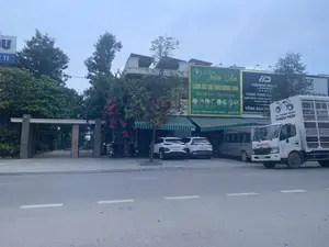 Bức ảnh chụp một con đường tại một khu đô thị, có thể là ở thị trấn Quán Lào, Yên Định, Thanh Hóa, dựa trên thông tin từ biển hiệu. Cảnh vật bao gồm các tòa nhà nhiều tầng ven đường, cây xanh và nhiều loại phương tiện.。Các biển hiệu có thể đọc được bao gồm:。- Biển hiệu màu xanh lá cây của 'Tâm An - CHĂM SÓC SỨC KHỎE DƯỠNG SINH' với khẩu hiệu 'Khỏe bên trong - Đẹp bên ngoài', ghi địa chỉ 'Lô 2 khu 4 - Thị trấn Quán Lào - Yên Định - Thanh Hóa' và số điện thoại '0917 617 468'.。- Biển hiệu màu đen của 'HOANG DONG LIMOUSINE' với các thông tin về hành trình và hợp đồng hành khách tuyến 'THANH HÓA - HÀ NỘI'.。- Trên một chiếc xe tải trắng có dòng chữ 'HỆ THỐNG HEAD THIỆU YÊN' và thương hiệu 'HONDA'.。- Một biển hiệu màu xanh dương bị che khuất một phần có chữ '...TẾ'.。Các vật thể và phương tiện trong ảnh:。- Một chiếc xe tải HONDA màu trắng.。- Một chiếc xe van màu bạc.。- Hai chiếc ô tô con màu trắng (một chiếc VinFast và một chiếc Hyundai).。- Một vài chiếc xe máy đang đậu trên vỉa hè.。- Các tòa nhà, một trong số đó có mái hiên sọc xanh trắng và một tòa nhà khác có lắp các tấm pin mặt trời trên mái.。- Cây cối và một giàn hoa giấy màu hồng.。- Một con đường nhựa có vạch kẻ đường màu trắng.。Hoạt động: Khung cảnh tĩnh, chủ yếu là các phương tiện đang đỗ trước các cửa hàng và nhà ở. Không có hoạt động cụ thể của con người được ghi lại.。（日本語訳）。写真は、看板の情報に基づき、おそらくタインホア省イエンディン県クアンラオ町にある都市部の一本の道を写したものです。風景には、道沿いの多層階の建物、緑の木々、そして多くの種類の乗り物が含まれています。読み取れる看板には以下が含まれます：。- 「タムアン - 養生ヘルスケア（Tâm An - CHĂM SÓC SỨC KHỎE DƯỠNG SINH）」の緑色の看板。「内側から健康に - 外側から美しく（Khỏe bên trong - Đẹp bên ngoài）」というスローガンがあり、住所「タインホア省イエンディン県クアンラオ町第4区2区画（Lô 2 khu 4 - Thị trấn Quán Lào - Yên Định - Thanh Hóa）」と電話番号「0917 617 468」が記載されています。- 「ホアン・ドン・リムジン（HOANG DONG LIMOUSINE）」の黒色の看板。「タインホア - ハノイ（THANH HÓA - HÀ NỘI）」路線の旅客の旅程と契約に関する情報が記載されています。- 一台の白いトラックには、「ティエウイエンHEADシステム（HỆ THỐNG HEAD THIỆU YÊN）」という文字と「HONDA」のブランド名があります。- 一部が隠れている青い看板に「...TẾ」という文字があります。写真の中の物体と乗り物：。- 一台の白いHONDAのトラック。- 一台の銀色のバン。- 二台の白い乗用車（一台はVinFast、もう一台はHyundai）。- 歩道に停まっている数台のバイク。- 複数の建物。そのうちの一つには青と白の縞模様の庇があり、別の建物には屋根にソーラーパネルが設置されています。- 木々とピンク色のブーゲンビリアの棚。- 白い車線が引かれたアスファルトの道路。活動：静かな光景で、主に店や家の前に乗り物が駐車しています。人間の具体的な活動は記録されていません。