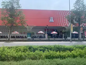 Bức ảnh chụp mặt tiền của một tòa nhà thương mại lớn, sơn màu đỏ. Trên tòa nhà có logo của chuỗi cửa hàng đồ ăn nhanh "KFC". Phía trước tòa nhà là khu vực để xe với nhiều xe máy đang đậu. Có một số chiếc ô (dù) che nắng màu đỏ và trắng. Cây xanh được trồng ở phía trước và hai bên. Các dòng chữ có thể nhận dạng được bao gồm: logo "KFC", chữ "KÍNH CHÀO" ở lối vào, và một tấm biển quảng cáo cho "Thea Coffee" với nội dung "TRONG SIÊU THỊ CÓ QUÁN CÀ PHÊ - TRÀ SỮA" và số hotline "0848.535.888". Ngoài ra còn có các chữ "SIÊU THỊ" và "ĂN NHANH" nhưng chỉ nhìn thấy một phần. Khung cảnh cho thấy đây là một khu vực thương mại, có thể là một siêu thị hoặc trung tâm mua sắm.。（日本語訳）。赤く塗られた大きな商業ビルの正面を撮影した写真です。建物にはファストフードチェーン「KFC」のロゴがあります。建物の前は駐車場で、多くのバイクが停まっています。赤と白の日よけの傘がいくつかあります。正面と両脇には緑の木が植えられています。認識できる文字には、「KFC」のロゴ、入口にある「KÍNH CHÀO」（いらっしゃいませ）の文字、そして「Thea Coffee」の広告看板が含まれます。看板には「TRONG SIÊU THỊ CÓ QUÁN CÀ PHÊ - TRÀ SỮA」（スーパーマーケット内にカフェ - ミルクティー店あり）という内容とホットライン番号「0848.535.888」が記載されています。その他に、「SIÊU THỊ」（スーパーマーケット）と「ĂN NHANH」（ファストフード）という文字もありますが、一部しか見えません。この光景は、ここが商業エリアであり、スーパーマーケットまたはショッピングセンターである可能性を示しています。