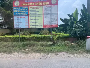 Bối cảnh là một khu vực ngoài trời, có thể là ven một con đường. Đối tượng chính trong ảnh là một tấm biển quảng cáo lớn thông báo tuyển dụng của Công ty TNHH May Phúc Linh. Xung quanh tấm biển là cây cối, bụi rậm và một vài cây chuối. Phía trên là bầu trời xanh có mây. Hoạt động chính được thể hiện là hoạt động tuyển dụng lao động thông qua biển báo.。Nội dung chi tiết trên biển quảng cáo được ghi lại như sau:。Tiêu đề: CÔNG TY TNHH MAY PHÚC LINH - THÔNG BÁO TUYỂN DỤNG.。Mức lương và thưởng:。- Lương sản phẩm: 7 - 20 triệu/tháng.。- Thưởng Tết (lương tháng 13) theo % tổng thu nhập cả năm, từ 6 - 30 triệu đồng/người.。- Thưởng vàng 9999 vào cuối năm.。Vị trí tuyển dụng:。- Công nhân may: 300 người。- Kỹ thuật: 02 người。- Công nhân kiểm hàng: 10 người。- Công nhân gấp gói, đóng thùng: 10 người。- Công nhân là: 05 người。- Công nhân BP cắt: 05 người。Chế độ cho công nhân may mới và người giới thiệu:。- Đối với công nhân mới: Thưởng 1.000.000đ vào lương tháng đầu tiên, đóng BHXH ngay, được hưởng nối thâm niên, hỗ trợ lương tới 03 tháng nếu không đạt lương sản lượng.。- Đối với người giới thiệu: Thưởng 1.000.000đ sau khi công nhân mới làm được 3 tháng, và các mức thưởng 3.000.000đ, 6.000.000đ, 10.000.000đ nếu giới thiệu được tương ứng 05, 10, 15 công nhân may/tháng.。Chế độ chung cho công nhân:。- Các khoản phụ cấp: Chuyên cần (500.000đ), Xăng xe (260.000đ), Thâm niên (từ 100.000 - 500.000đ), Hỗ trợ phụ nữ (30.000đ), Hỗ trợ nuôi con nhỏ (100.000đ/cháu/tháng), Cơm ca (442.000/tháng), Hỗ trợ chủ nhật (100.000đ/ngày), Hỗ trợ tăng ca sau 16h30 (260.000/tháng).。- Quyền lợi: Hưởng đầy đủ chế độ BHXH-BHYT, hưởng lễ tết, phép năm, lương trả vào ngày 15 hàng tháng, tham quan du lịch hàng năm, tổ chức sinh nhật tháng, tặng quà các ngày lễ (8/3, 1/6, Tết Trung Thu, 20/10), tham gia giao lưu ca nhạc hàng tuần.。Thông tin liên hệ:。- Liên hệ: Ms. Huệ 0949 752 726 - Ms. Bình 0838 346 999.。- Fanpage: Công ty TNHH may Phúc Linh.。- Địa chỉ: Thôn Ấp Trú - Định Bình - Yên Định - Thanh Hoá.。（日本語訳）。背景は屋外で、おそらく道端です。写真の主な対象物は、フックリン縫製有限会社の求人募集を告知する大きな広告看板です。看板の周りには木々、茂み、そして数本のバナナの木があります。上には雲のある青空が広がっています。示されている主な活動は、看板を通じた労働者の採用活動です。広告看板の詳細な内容は以下の通りです。見出し：フックリン縫製有限会社 - 採用募集のお知らせ。給与と賞与：。- 出来高給：月700万～2000万ドン。- テト賞与（13ヶ月目の給与）は年間総収入の％に基づき、一人当たり600万～3000万ドン。- 年末に9999ゴールドの賞与あり。募集職種：。- 縫製工：300名。- 技術者：02名。- 検品作業員：10名。- 梱包・箱詰め作業員：10名。- アイロンがけ作業員：05名。- 裁断部門作業員：05名。新規縫製工と紹介者向けの制度：。- 新規作業員向け：初月の給与に1,000,000ドンの賞与、社会保険即時加入、勤続年数の継続適用、出来高給に達しない場合は最大3ヶ月間の給与補助。- 紹介者向け：新規作業員が3ヶ月勤務後に1,000,000ドンの賞与。また、月にそれぞれ5名、10名、15名の縫製工を紹介した場合、3,000,000ドン、6,000,000ドン、10,000,000ドンの賞与。全作業員向けの共通制度：。- 各種手当：皆勤手当（500,000ドン）、交通費（260,000ドン）、勤続手当（100,000～500,000ドン）、女性支援手当（30,000ドン）、育児支援手当（子供一人当たり月100,000ドン）、食事手当（月442,000ドン）、日曜出勤手当（日100,000ドン）、16時30分以降の残業手当（月260,000ドン）。- 権利・福利厚生：社会保険・医療保険制度の完全適用、祝祭日・年次休暇の取得、給与は毎月15日払い、毎年の社員旅行、月例誕生日会、祝日（3月8日、6月1日、中秋節、10月20日）のプレゼント贈呈、毎週の音楽交流会への参加。連絡先情報：。- 連絡先：フエさん 0949 752 726 - ビンさん 0838 346 999。- ファンページ：フックリン縫製有限会社。- 住所：タインホア省イエンディン県ディンビン社アップチュー村。