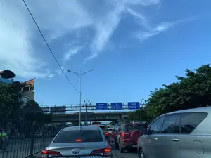 Bức ảnh được chụp từ bên trong một chiếc ô tô, ghi lại cảnh giao thông đông đúc trên một con đường ở Việt Nam, có thể là lối vào một tuyến đường cao tốc hoặc một nút giao thông quan trọng. Nhiều xe ô tô đang dừng hoặc di chuyển chậm thành hàng dài, cho thấy tình trạng ùn tắc. Phía trên có một cây cầu vượt hoặc đường trên cao. Bầu trời trong xanh, có ít mây, cho thấy thời tiết đẹp.。Các thông tin bằng chữ trên các biển báo chỉ đường lớn màu xanh lam có thể được ghi lại như sau:。- Biển báo chỉ hướng bên trái: "CT PHÁP VÂN CẦU GIẼ 0,5 km", "CẦU THANH TRÌ 8.5 km".。- Biển báo chỉ hướng đi thẳng: "ĐƯỜNG NGỌC HỒI", "UBND HUYỆN THANH TRÌ 2,3 km", "ĐƯỜNG PHAN TRỌNG TUỆ 2,6 km".。- Biển báo chỉ hướng bên phải: "PHỐ HOÀNG LIỆT", "KHU ĐÔ THỊ LINH ĐÀM 1 km".。Các vật thể khác trong ảnh bao gồm nhiều loại ô tô khác nhau, cây xanh hai bên đường, các tòa nhà, và một cột đèn đường. Hoạt động chính là các phương tiện đang tham gia giao thông trên đường.。（日本語訳）。写真は車内から撮影されたもので、ベトナムのある道路の混雑した交通風景を記録しており、高速道路の入口か主要な交差点の可能性があります。多くの自動車が停止またはゆっくりと長い列を作って移動しており、渋滞状況を示しています。上方には陸橋または高架道路があります。空は青く澄んでおり、雲は少なく、天気が良いことを示しています。大きな青い道路標識に書かれた文字情報は以下の通りです。- 左方向の標識：「CT PHÁP VÂN CẦU GIẼ 0,5 km」、「CẦU THANH TRÌ 8.5 km」。- 直進方向の標識：「ĐƯỜNG NGỌC HỒI」、「UBND HUYỆN THANH TRÌ 2,3 km」、「ĐƯỜNG PHAN TRỌNG TUỆ 2,6 km」。- 右方向の標識：「PHỐ HOÀNG LIỆT」、「KHU ĐÔ THỊ LINH ĐÀM 1 km」。写真の中の他の物体には、様々な種類の自動車、道路の両側の緑の木々、建物、そして街灯が含まれます。主な活動は、車両が道路で交通に参加していることです。