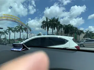 Bức ảnh được chụp từ bên trong một chiếc ô tô, nhìn ra một ngã tư đường phố vào một ngày nắng đẹp với trời xanh và mây trắng. Ở phía trước là một cổng chào lớn bằng kim loại màu đỏ, trên đó có dòng chữ màu vàng: "PHỐ ĐI BỘ PHAN CHU TRINH" và "KHÔNG GIAN VĂN HÓA QUẢNG TRƯỜNG LAM SƠN". Nhiều ô tô, bao gồm cả taxi, đang dừng chờ đèn đỏ trên đường. Hai bên đường và trong khu vực quảng trường có trồng nhiều cây cọ cao. Ở phía sau, có thể thấy một tòa nhà lớn mang kiến trúc cổ điển. Trên tòa nhà này có treo một biểu ngữ màu xanh lá cây với nội dung có thể đọc được một phần: "...NHÀ, GIẢI NGÂN, THU NỢ TẠI XÃ...". Cảnh vật cho thấy đây là một khu vực trung tâm của thành phố.。（日本語訳）。写真は車内から撮影されたもので、青空と白い雲が広がる晴れた日に、街の交差点を見渡しています。前方には大きな赤い金属製の歓迎ゲートがあり、その上には黄色い文字で「PHỐ ĐI BỘ PHAN CHU TRINH」と「KHÔNG GIAN VĂN HÓA QUẢNG TRƯỜNG LAM SƠN」と書かれています。タクシーを含む多くの車が、道路で赤信号を待っています。道路の両側と広場エリアには、多くの背の高いヤシの木が植えられています。後方には、古典的な建築様式の大きな建物が見えます。この建物には緑色の横断幕が掲げられており、その内容は「...NHÀ, GIẢI NGÂN, THU NỢ TẠI XÃ...」と一部読み取ることができます。この風景は、ここが市の中心部であることを示しています。