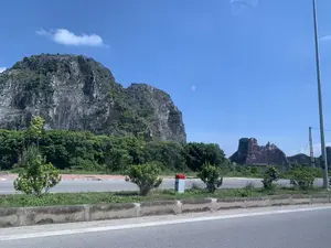 Bức ảnh chụp một con đường lớn với những dãy núi đá vôi hùng vĩ ở phía sau, có khả năng được chụp tại tỉnh Thanh Hóa. Bầu trời trong xanh và quang đãng. Cảnh vật chính bao gồm: một con đường nhựa rộng, một dải phân cách ở giữa có trồng cây xanh, và những ngọn núi đá vôi đặc trưng. Bên lề đường có một cột mốc kilômét bằng bê tông, sơn hai màu trắng và đỏ, trên đó có ghi chữ "H7" và số "0". Phía xa, một người đang lái xe máy. Cây cối xanh tươi mọc ở chân núi và trên dải phân cách. Một phần của ngọn núi ở xa dường như là một công trường khai thác đá.。（日本語訳）。背景に雄大な石灰岩の山脈が連なる大きな道路を写した写真で、おそらくタインホア省で撮影されたものです。空は青く澄み渡っています。主な風景は、広いアスファルトの道路、緑の木々が植えられた中央分離帯、そして特徴的な石灰岩の山々です。道端にはコンクリート製のキロポストがあり、白と赤の2色で塗られ、「H7」という文字と「0」という数字が書かれています。遠くには、バイクを運転している人が一人います。青々とした木々が山の麓や中央分離帯に生えています。遠くの山の一部は、採石場のようです。