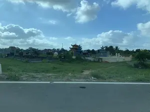 Bức ảnh chụp một khu nghĩa trang ven đường ở một vùng nông thôn. Trong ảnh có nhiều ngôi mộ và lăng mộ với các kích thước và kiểu dáng kiến trúc khác nhau. Một số lăng mộ được xây dựng rất công phu, có mái cong nhiều tầng theo phong cách truyền thống, trong khi những ngôi mộ khác thì đơn giản hơn. Khu vực nghĩa trang có nhiều cỏ mọc. Ở phía sau có thể thấy cây cối và đường dây điện. Bầu trời trong xanh, có nhiều mây trắng. Phần tiền cảnh là mặt đường nhựa, cho thấy bức ảnh có thể được chụp từ một phương tiện đang di chuyển. Không có hoạt động nào của con người diễn ra. Không có văn bản nào có thể đọc được.。（日本語訳）。写真は、ある田舎の道端にある墓地を写したものです。一部の霊廟は非常に精巧に建てられており、伝統的な様式の多層の湾曲した屋根を持っていますが、他の墓はより簡素です。墓地エリアには草がたくさん生えています。後方には木々や電線が見えます。空は青く、白い雲がたくさん浮かんでいます。前景はアスファルトの路面で、写真が移動中の乗り物から撮影された可能性があることを示しています。人間の活動は見られません。読み取れる文字はありません。