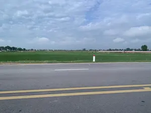 Bức ảnh chụp một con đường nhựa ở vùng nông thôn. Mặt đường có vạch kẻ đôi liền màu vàng và một vạch kẻ đơn màu trắng. Bên lề đường có một cọc tiêu giao thông sơn màu trắng và đỏ. Cạnh con đường là một cánh đồng lúa rộng lớn, xanh mướt. Ở phía xa là khung cảnh của một làng quê với cây cối và nhà cửa. Bầu trời nhiều mây. Không có hoạt động cụ thể nào của con người được ghi lại, chỉ là một khung cảnh yên tĩnh đặc trưng của vùng nông thôn. Không có văn bản hay chữ viết nào trong ảnh.。（日本語訳）。写真は、田舎にあるアスファルトの道路を写したものです。路面には黄色の二重実線と白色の一本線が引かれています。路肩には、白と赤に塗られた視線誘導標が一本立っています。道路の隣には、広大で青々とした水田が広がっています。遠方には、木々や家々のある村の風景が見えます。空は雲が多いです。特定の人間活動は記録されておらず、田舎に特有の静かな風景が広がっているだけです。写真の中にテキストや文字はありません。