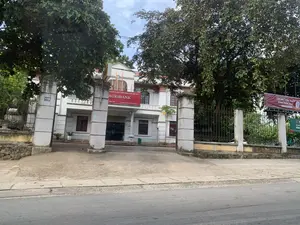 Bức ảnh chụp quang cảnh bên ngoài của một tòa nhà hai tầng, là trụ sở của một chi nhánh ngân hàng. Phía trước tòa nhà là một con đường nhựa. Tòa nhà được sơn màu trắng, có cổng vào với hai cột trụ lớn màu trắng và hàng rào sắt. Trên một cột trụ có gắn biển số nhà "145". Ở trung tâm mặt tiền tòa nhà có một biển hiệu lớn màu đỏ với dòng chữ "NGÂN HÀNG NÔNG NGHIỆP VÀ PHÁT TRIỂN NÔNG THÔN VIỆT NAM", "AGRIBANK", và địa chỉ "Địa chỉ: Xã Yên Trường, Huyện Yên Định, Tỉnh Thanh Hóa". Trên nóc nhà có cắm hai lá cờ đỏ, trong đó có quốc kỳ Việt Nam. Bên phải, có một băng rôn màu đỏ quảng cáo về "CÀI ĐẶT THU THẬP SINH TRẮC HỌC". Xung quanh khuôn viên có nhiều cây xanh lớn. Khung cảnh tĩnh lặng, không có hoạt động nào của con người được ghi lại.。（日本語訳）。写真は、銀行の一支店の本部である、2階建ての建物の外観を写したものです。建物の前はアスファルトの道路です。建物は白く塗られており、2本の大きな白い柱と鉄柵のある入口ゲートがあります。一本の柱には「145」という番地プレートが取り付けられています。建物の正面中央には、「NGÂN HÀNG NÔNG NGHIỆP VÀ PHÁT TRIỂN NÔNG THÔN VIỆT NAM」、「AGRIBANK」、そして住所「Địa chỉ: Xã Yên Trường, Huyện Yên Định, Tỉnh Thanh Hóa」という文字が入った大きな赤い看板があります。屋根の上には2本の赤い旗が掲げられており、その中にはベトナム国旗が含まれています。右側には、「CÀI ĐẶT THU THẬP SINH TRẮC HỌC」を宣伝する赤い横断幕があります。敷地の周りには多くの大きな緑の木があります。風景は静かで、人の活動は記録されていません。