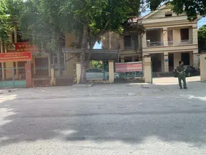 Bối cảnh là phía trước một tòa nhà công vụ, cụ thể là trụ sở Công an huyện Thiệu Hóa, tỉnh Thanh Hóa. Một người đàn ông mặc sắc phục công an màu xanh lá cây đang đứng trong sân của tòa nhà. Phía trước là một con đường nhựa, vỉa hè, và một hàng rào sắt bao quanh khuôn viên. Có nhiều cây xanh và một vài chiếc ô tô đang đỗ bên trong. Các biển hiệu và băng rôn màu đỏ có ghi các thông tin sau:。1. Biển hiệu lớn có biểu tượng công an: "HỌC TẬP VÀ LÀM THEO TƯ TƯỞNG, ĐẠO ĐỨC, PHONG CÁCH HỒ CHÍ MINH".。2. Biển hiệu bên dưới: "CÔNG AN HUYỆN THIỆU HÓA", "ĐỘI CẢNH SÁT GIAO THÔNG - TRẬT TỰ", "BỘ PHẬN TIẾP DÂN CẤP ĐĂNG KÝ, BIỂN SỐ PHƯƠNG TIỆN GIAO THÔNG CƠ GIỚI ĐƯỜNG BỘ VÀ XỬ PHẠT VI PHẠM HÀNH CHÍNH LĨNH VỰC TRẬT TỰ AN TOÀN GIAO THÔNG".。3. Băng rôn treo trên hàng rào: "CÔNG AN HUYỆN THIỆU HÓA, TỈNH THANH HÓA", "ĐIỂM HỖ TRỢ, GIÚP ĐỠ NGƯỜI DÂN VỀ QUÊ ĐÓN TẾT".。4. Trên cột cổng bằng gạch có ghi số nhà là "306".。（日本語訳）。背景は官公庁の建物の前で、具体的にはタインホア省ティエウホア県警察署です。緑色の警察制服を着た一人の男性が、建物の敷地内に立っています。前方にはアスファルトの道路、歩道、そして敷地を囲む鉄の柵があります。多くの緑の木があり、数台の車が中に駐車しています。赤色の看板と横断幕には、以下の情報が書かれています。1. 警察のシンボルマークが付いた大きな看板：「ホーチミンの思想、道徳、風格を学び、それに従う」。2. 下の看板：「ティエウホア県警察」、「交通警察・秩序隊」、「道路自動車交通手段の登録・ナンバープレート交付及び交通安全秩序分野における行政違反の処罰に関する市民受付部門」。3. 柵に掛けられた横断幕：「タインホア省ティエウホア県警察」、「テト（旧正月）を迎えるために帰省する人々を支援・援助する拠点」。4. レンガ造りの門柱には「306」という番地が書かれています。