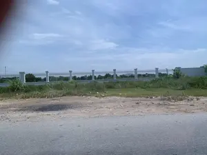 Đây là một khung cảnh ven đường. Phía trước là một con đường nhựa, bên cạnh là lề đường bằng đất có cỏ dại mọc và một ít rác. Ở phía sau là một hàng rào dài được xây bằng các cột trụ bê tông và lan can sắt. Bên trong hàng rào là một khu đất có nhiều cây cối. Bầu trời trong xanh và có mây. Không có người hay hoạt động nào đang diễn ra. Không có văn bản hay biển báo nào trong ảnh.。（日本語訳）。これは道端の光景です。手前にはアスファルトの道があり、その隣には雑草が生え、少しゴミが落ちている土の路肩があります。後方には、コンクリートの柱と鉄柵で建てられた長いフェンスがあります。フェンスの内側は、たくさんの木々がある土地です。空は青く澄んでおり、雲があります。人や、行われている活動はありません。写真の中には、文字や標識はありません。