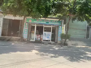 Hình ảnh chụp một hiệu thuốc ven đường vào ban ngày. Biển hiệu chính lớn có nền màu xanh lá cây và chữ màu trắng, vàng, ghi rõ: "QUẦY THUỐC SỐ 5", "BÁN LẺ THUỐC", "THÀNH PHẨM". Phía trên biển hiệu có các thông tin khác như "CÔNG TY CỔ PHẦN DƯỢC... CHI NHÁNH DƯỢC PHẨM ĐÔNG SƠN", địa chỉ "SỐ NHÀ 82 - KHỐI 3 - THỊ TRẤN RỪNG THÔNG" và số điện thoại. Hai bên cửa ra vào có các biển hiệu dọc màu xanh ghi "QUẦY THUỐC ĐẠT TIÊU CHUẨN GPP". Trên cửa kính có dán một tấm áp phích quảng cáo sản phẩm "SUBAVAX" dùng để xịt mũi họng. Khung cảnh là một con đường nhựa, có những cây xanh lớn tỏa bóng mát. Hiệu thuốc có vẻ đang mở cửa. Cửa hàng bên phải thì đóng cửa cuốn màu xanh, trong khi cửa hàng bên trái mở cửa và có một chiếc xe máy đỗ bên trong.。（日本語訳）。昼間に撮影された道端の薬局の写真。大きなメイン看板は緑色の背景に白と黄色の文字で、「QUẦY THUỐC SỐ 5」（5番薬局カウンター）、「BÁN LẺ THUỐC」（医薬品小売）、「THÀNH PHẨM」（完成品）と明記されている。看板の上部には、「CÔNG TY CỔ PHẦN DƯỢC... CHI NHÁNH DƯỢC PHẨM ĐÔNG SƠN」（...製薬株式会社 ドンソン医薬品支店）、住所「SỐ NHÀ 82 - KHỐI 3 - THỊ TRẤN RỪNG THÔNG」（ルン・トン町 3区 82番地）、そして電話番号といった他の情報がある。出入り口の両側には、「QUẦY THUỐC ĐẠT TIÊU CHUẨN GPP」（GPP基準適合薬局カウンター）と書かれた緑色の縦長の看板がある。ガラスのドアには、鼻・喉用のスプレー製品「SUBAVAX」を宣伝するポスターが貼られている。風景はアスファルトの道で、大きな緑の木々が涼しい木陰を作っている。薬局は営業しているようだ。右隣の店は青いシャッターが閉まっているが、左隣の店は開いており、中にバイクが1台停まっている。