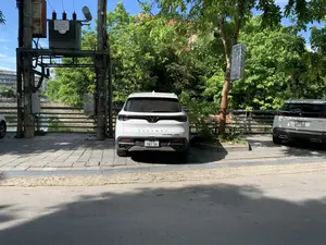 Bối cảnh là một con đường có vỉa hè lát gạch, nơi có hai chiếc ô tô đang đỗ. Ở vị trí trung tâm là một chiếc SUV màu trắng hiệu VinFast LUX SA2.0 Turbo. Một phần của chiếc SUV Peugeot 3008 màu trắng khác cũng có thể được nhìn thấy ở bên phải. Những chiếc xe này đỗ bên cạnh một con kênh nhỏ có bờ kè bê tông và lan can sắt. Xung quanh có nhiều cây xanh tươi tốt và một cột điện với trạm biến áp.。Các thông tin bằng chữ có thể nhận dạng bao gồm:。- Trên trạm biến áp có biển ghi: "CÔNG TY ĐIỆN LỰC THANH HÓA", "TRẠM BIẾN ÁP", "CÔNG TY THIỆN XUÂN", và thông số kỹ thuật "75KVA - 22/0,4KV".。- Treo trên một thân cây là biển chỉ dẫn của một nhà hàng với dòng chữ "NHÀ HÀNG HÀN QUỐC" và chữ Hàn Quốc "레스토랑" cùng một mũi tên chỉ hướng.。- Trên chiếc xe có các chữ "VINFAST" và "LUX SA2.0 TURBO".。- Một tấm biển nhỏ màu đỏ gần hàng rào có chữ "...COM" và "TƯ VẤN CHỨNG CHỈ TIẾNG ANH CHO BẠN" nhưng bị che khuất một phần.。Không có hoạt động nào của con người được ghi lại trong ảnh, chỉ có những chiếc xe đang đỗ.。（日本語訳）。背景は、2台の車が駐車しているレンガ敷きの歩道がある道路です。中央には、VinFast LUX SA2.0 Turboブランドの白いSUVが1台あります。右側には、別の白いSUV、Peugeot 3008の一部も見えます。これらの車は、コンクリートの護岸と鉄の手すりがある小さな水路の隣に駐車しています。周りには青々とした多くの木々と、変電設備付きの電柱が1本あります。認識できる文字情報は以下の通りです。- 変電設備には、「CÔNG TY ĐIỆN LỰC THANH HÓA」（タインホア電力会社）、「TRẠM BIẾN ÁP」（変電所）、「CÔNG TY THIỆN XUÂN」（ティエンスアン社）、および技術仕様「75KVA - 22/0,4KV」と書かれた看板があります。- 木の幹には、「NHÀ HÀNG HÀN QUỐC」（韓国レストラン）という文字と韓国語の「레스토랑」（レストラン）、そして方向を示す矢印が書かれたレストランの案内看板が掛けられています。- 車には「VINFAST」と「LUX SA2.0 TURBO」という文字があります。- フェンスの近くにある小さな赤い看板には、「...COM」と「TƯ VẤN CHỨNG CHỈ TIẾNG ANH CHO BẠN」（あなたのための英語資格証明書コンサルティング）という文字がありますが、一部が隠れています。