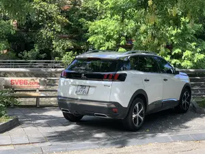 Bức ảnh chụp một chiếc ô tô SUV màu trắng, hiệu Peugeot 3008, đang đỗ trên một khu vực vỉa hè được lát bằng gạch vuông. Bối cảnh phía sau là cây cối xanh tươi rậm rạp, trong đó có cây hoa muồng hoàng yến với những chùm hoa màu vàng. Phía sau xe, có một chiếc ghế đá bằng bê tông. Trên phần tựa lưng của ghế có sơn dòng chữ quảng cáo màu đỏ 'SV66.com' và một dòng chữ nhỏ hơn 'NƠI GIẢI TRÍ DANH... CHO BẠN'. Gần đó còn có lan can bê tông. Toàn bộ khung cảnh cho thấy đây là một không gian công cộng hoặc ven đường ở một khu đô thị. Trên đuôi xe có ghi thương hiệu 'PEUGEOT' và model '3008'.。（日本語訳）。写真は、プジョー3008というブランドの白いSUV車が、四角いタイルで舗装された歩道の一角に駐車しているところを写したものです。背景には青々と生い茂る木々があり、その中には黄色い花の房をつけたゴールデンシャワー（ムオン・ホアン・イエン）の木があります。車の後ろには、コンクリート製の石のベンチがあります。ベンチの背もたれには、「SV66.com」という赤い広告文と、それより小さな「NƠI GIẢI TRÍ DANH... CHO BẠN」という文が塗装されています。その近くにはコンクリート製の手すりもあります。全体の光景は、ここが都市部の公共空間または道端であることを示しています。車の後部には、ブランド名「PEUGEOT」とモデル名「3008」が記されています。