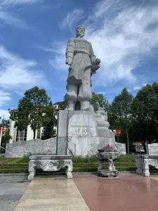 Đây là hình ảnh chụp một tượng đài lớn bằng đá tại một quảng trường hoặc khu tưởng niệm ngoài trời. Bức tượng khắc họa một nhân vật lịch sử trong trang phục võ tướng, đứng hiên ngang trên bệ đá cao. Trên bệ tượng có khắc dòng chữ màu vàng: 'ANH HÙNG DÂN TỘC LÊ LỢI 1385 - 1433'. Phía trước tượng đài có một lư hương lớn bằng đá và các bàn đá được chạm khắc hoa văn. Bên trong lư hương có nhiều chân hương, cho thấy đây là nơi người dân đến để thắp hương tưởng niệm. Xung quanh tượng đài là cây xanh, các bức tường có phù điêu đá. Phía sau có thể thấy một tòa nhà hiện đại và cờ Việt Nam. Bối cảnh là một ngày nắng đẹp với bầu trời trong xanh và mây trắng.。（日本語訳）。これは、屋外の広場または記念区域にある大きな石の記念碑を撮影した写真です。像は、武将の衣装をまとった歴史上の人物が、高い石の台座の上に堂々と立っている様子を描いています。像の台座には、「民族の英雄 レ・ロイ 1385 - 1433」という金色の文字が刻まれています。記念碑の前には、大きな石の香炉と、模様が彫刻された石の台があります。香炉の中には多くの線香の燃え差しがあり、ここが人々が追悼のために線香を焚きに来る場所であることを示しています。記念碑の周りには緑の木々や、石のレリーフがある壁があります。後方には、近代的な建物とベトナムの国旗が見えます。背景は、青く澄んだ空と白い雲が広がる、晴れた美しい日です。
