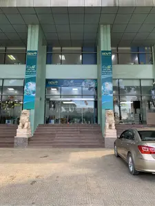 Bức ảnh chụp lối vào chính của một tòa nhà văn phòng hiện đại, là một chi nhánh của Ngân hàng BIDV. Phía trước tòa nhà là một cầu thang rộng bằng đá dẫn lên cửa ra vào tự động bằng kính. Hai bên cầu thang có hai bức tượng sư tử đá được đặt trên bệ. Các cột trụ lớn của tòa nhà được treo các biểu ngữ (banner) dọc và ngang để kỷ niệm 67 năm thành lập. Nội dung trên các biểu ngữ bao gồm logo 'BIDV', khẩu hiệu 'Vững bước Tiên phong - Đồng hành Phát triển', và dòng chữ 'Tự hào 67 năm PHÁT TRIỂN CÙNG ĐẤT NƯỚC' cùng mốc thời gian '26/4/1957 - 26/4/2024'. Qua cửa kính, có thể nhìn thấy không gian giao dịch bên trong với bàn ghế và một vài người. Ở phía bên phải, một chiếc ô tô màu vàng đồng đang đỗ trên sân được lát gạch.。（日本語訳）。近代的なオフィスビルの正面玄関を撮影した写真で、BIDV銀行の支店です。ビルの正面には、ガラス製の自動ドアへと続く、幅の広い石の階段があります。階段の両脇には、台座の上に置かれた2体の石の獅子の像があります。ビルの大きな柱には、創立67周年を記念する縦横の横断幕（バナー）が掲げられています。横断幕の内容には、「BIDV」のロゴ、スローガン「先駆者として着実に歩み、発展と共に歩む」、そして「国と共に発展した誇り高き67年」という文言と「1957年4月26日 - 2024年4月26日」の期間が含まれています。ガラスのドア越しに、内部の取引スペースに机や椅子、そして数人の人々が見えます。右側には、タイル張りの敷地にブロンズ色の車が1台駐車しています。