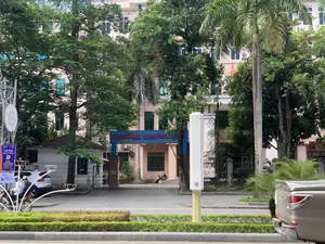 Hình ảnh chụp cổng vào của một tòa nhà trụ sở cơ quan nhà nước tại thành phố Thanh Hóa. Trên cổng có một biển hiệu lớn màu xanh với nội dung: 'SỞ NỘI VỤ TỈNH THANH HÓA. BAN TÔN GIÁO - CHI CỤC VĂN THƯ LƯU TRỮ. ĐT: 02373.717.094 - ĐT: 02373.728.955. ĐỊA CHỈ: SỐ 45A ĐẠI LỘ LÊ LỢI - PHƯỜNG LAM SƠN - THÀNH PHỐ THANH HÓA.' Tòa nhà chính là một công trình nhiều tầng, được bao quanh bởi nhiều cây xanh tươi tốt, có thể thấy cả cây phượng và cây cọ. Một lá cờ Việt Nam (cờ đỏ sao vàng) được treo trên tòa nhà. Bên trong sân, có một bốt bảo vệ và một chiếc xe máy đang đỗ. Phía trước là một con đường nhựa, có người đang điều khiển xe máy lưu thông. Một chiếc ô tô màu trắng đang đỗ bên lề đường. Bên trái có treo một băng rôn màu tím với nội dung 'CHÀO MỪNG ĐẠI BIỂU THAM DỰ LIÊN HOAN PHÁT THANH TOÀN QUỐC LẦN THỨ XVI - 2024'.。（日本語訳）。タインホア市にある国家機関の本庁舎の入り口の門を撮影した写真。門の上には大きな青い看板があり、内容は「タインホア省内務局。宗教委員会 - 公文書・アーカイブ支局。電話：02373.717.094 - 電話：02373.728.955。住所：タインホア市ラムソン坊レロイ大通り45A番地」。敷地内には、警備員の詰所と駐車しているバイクが1台ある。前方にはアスファルトの道路があり、バイクを運転して通行している人がいる。1台の白い自動車が道路脇に駐車している。