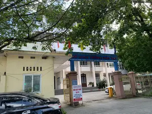 Bức ảnh chụp lối vào của một tòa nhà trụ sở cơ quan nhà nước, cụ thể là Sở Giao thông Vận tải tỉnh Thanh Hóa. Trên biển hiệu lớn màu xanh ở cổng có ghi: 'ỦY BAN NHÂN DÂN TỈNH THANH HÓA - SỞ GIAO THÔNG VẬN TẢI'. Phía dưới là thông tin liên hệ: 'Đ/C: 42 Đại Lộ Lê Lợi - P. Điện Biên - TP. Thanh Hóa * ĐT: 0373.852 360 - Fax: 0373.855 129 * Website: sgtvt.thanhhoa.gov.vn - Email: sgtvt@thanhhoa.gov.vn'.。Tại cổng vào, có một biển 'THÔNG BÁO' màu trắng với chữ đỏ, nội dung về việc 'ĐỔI GIẤY PHÉP LÁI XE' đã 'CHUYỂN VỀ TRUNG TÂM PHỤC VỤ HÀNH CHÍNH CÔNG TỈNH THANH HÓA' tại địa chỉ 'Số: 28 Đại Lộ Lê Lợi, P. Điện Biên, TP. Thanh Hóa'. Phía trên là một biển nhỏ màu xanh yêu cầu: 'YÊU CẦU QUÝ KHÁCH XUỐNG XE XUẤT TRÌNH GIẤY TỜ'.。Khung cảnh cho thấy một tòa nhà hành chính nhiều tầng, sơn màu trắng và kem, nằm sau một hàng rào và cổng sắt. Phía trước có một chiếc ô tô màu đen đang đỗ. Bên trong sân có một barie tự động màu vàng và một phần chiếc ô tô khác. Phía trên cổng có treo nhiều lá cờ màu đỏ, vàng và xanh. Cây xanh có tán lá rộng che một phần tầm nhìn vào tòa nhà.。（日本語訳）。ある国家機関の本庁舎の入り口を写した写真で、具体的にはタインホア省交通運輸局である。門にある青い大きな看板には、「タインホア省人民委員会 - 交通運輸局」と書かれている。その下には連絡先情報がある：「住所：タインホア市ディエンビエン坊レロイ大通り42番地 ＊ 電話：0373.852 360 - ファックス：0373.855 129 ＊ ウェブサイト：sgtvt.thanhhoa.gov.vn - Eメール：sgtvt@thanhhoa.gov.vn」。入り口の門には、赤字で書かれた白い「お知らせ」の看板があり、その内容は「運転免許証の交換」業務が「タインホア省公共行政サービスセンター」へ「移転した」というもので、住所は「タインホア市ディエンビエン坊レロイ大通り28番地」である。その上には、「お客様は降車の上、書類を提示してください」と要求する小さな青い看板がある。風景は、鉄柵と鉄の門の後ろに位置する、白とクリーム色に塗られた多層階の行政庁舎を示している。前方には一台の黒い自動車が駐車している。葉が広く茂った緑の木が、建物への視界の一部を遮っている。