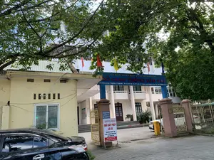 Bức ảnh chụp lối vào của Sở Giao thông Vận tải tỉnh Thanh Hóa. Phía trên cổng chính có một biển hiệu lớn màu xanh với dòng chữ: 'ỦY BAN NHÂN DÂN TỈNH THANH HÓA - SỞ GIAO THÔNG VẬN TẢI'. Bên dưới là thông tin địa chỉ và liên lạc: 'Đ/C: 42 Đại Lộ Lê Lợi - P. Điện Biên - TP. Thanh Hóa * ĐT: 0373.852 360 - Fax: 0373. 855 129 * Website: sgtvt.thanhhoa.gov.vn - Email: sgtvt.@thanhhoa.gov.vn'.。Tại cổng ra vào, có một biển báo nhỏ màu xanh trên cột cổng ghi: 'YÊU CẦU QUÝ KHÁCH XUỐNG XE XUẤT TRÌNH GIẤY TỜ'. Bên cạnh đó là một biển 'THÔNG BÁO' nền trắng chữ đỏ, với nội dung: 'ĐỔI GIẤY PHÉP LÁI XE CHUYỂN VỀ TRUNG TÂM PHỤC VỤ HÀNH CHÍNH CÔNG TỈNH THANH HÓA. Số: 28 Đại Lộ Lê Lợi, P. Điện Biên, TP. Thanh Hóa'.。Khung cảnh cho thấy một tòa nhà văn phòng nhiều tầng, phía trước có cây xanh lớn. Một chiếc ô tô màu đen đang đỗ ở phía trước bên trái. Có một rào chắn tự động (barie) ở lối vào và nhiều lá cờ được cắm trên tòa nhà.。（日本語訳）。タインホア省交通運輸局の入り口を写した写真です。正門の上には、「タインホア省人民委員会 - 交通運輸局」と書かれた大きな青い看板があります。その下には住所と連絡先情報があります：「住所：タインホア市ディエンビエン区レロイ大通り42番地 * 電話：0373.852 360 - ファックス：0373. 855 129 * ウェブサイト：sgtvt.thanhhoa.gov.vn - Eメール：sgtvt.@thanhhoa.gov.vn」。出入り口の門柱には、「お客様は降車の上、書類をご提示ください」と書かれた小さな青い標識があります。その隣には、白地に赤文字の「お知らせ」の看板があり、内容は「運転免許証の更新はタインホア省公共行政サービスセンターに移転しました。住所：タインホア市ディエンビエン区レロイ大通り28番地」です。風景には、多層階のオフィスビルが写っており、その前には大きな緑の木があります。左手前には黒い自動車が一台駐車しています。入り口には自動ゲート（遮断機）があり、建物には多くの旗が掲げられています。