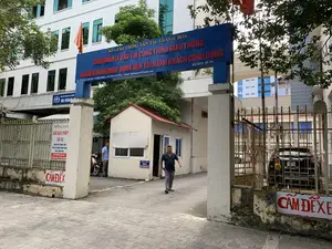 Bức ảnh chụp lối vào của một cơ quan nhà nước tại thành phố Thanh Hóa, cụ thể là trụ sở của Sở Giao thông Vận tải. Phía trên cổng ra vào có một tấm biển lớn màu xanh lam với dòng chữ đỏ và trắng. Dòng chữ trên cùng ghi "SỞ GIAO THÔNG VẬN TẢI THANH HÓA". Bên dưới là "BAN QUẢN LÝ BẢO TRÌ CÔNG TRÌNH GIAO THÔNG CÔNG CỘNG VÀ ĐIỀU HÀNH HOẠT ĐỘNG VẬN TẢI HÀNH KHÁCH CÔNG CỘNG", cùng với địa chỉ "ĐC: 13 HẠC THÀNH - P. ĐIỆN BIÊN - TP. THANH HÓA", email và số điện thoại "ĐT: 02373 515 516".。Cảnh vật cho thấy một tòa nhà văn phòng nhiều tầng màu trắng ở phía sau, có cờ Việt Nam và một lá cờ khác đang bay. Lối vào có một cổng sắt, một bốt bảo vệ nhỏ và một barie chắn. Một người đàn ông mặc áo phông sẫm màu đang đi bộ ra khỏi cổng. Bên trong, một người đàn ông khác đang đứng gần một chiếc xe máy. Một chiếc ô tô màu đen đang đỗ phía sau barie.。Trên các cột và tường có nhiều biển báo và thông báo khác nhau:。- Một tờ "THÔNG BÁO" dán trên cột thông báo việc "ĐỔI GIẤY PHÉP LÁI XE" đã chuyển về "TRUNG TÂM PHỤC VỤ HÀNH CHÍNH CÔNG TỈNH THANH HÓA" tại địa chỉ "Số: 28 Đại Lộ Lê Lợi, P. Điện Biên, TP. Thanh Hóa".。- Một biển nhỏ trên bốt bảo vệ ghi "YÊU CẦU XUỐNG XE XUẤT TRÌNH GIẤY TỜ".。- Dòng chữ "CẤM ĐỂ XE" được sơn màu đỏ trên bức tường thấp.。- Một biển hiệu khác có thể nhìn thấy một phần ghi "BAN AN TOÀN GIAO THÔNG" và "VĂN PHÒNG".。（日本語訳）。この写真はタインホア市にある国家機関の入り口を撮影したもので、具体的には交通運輸局の本庁舎です。出入り口の上には、赤と白の文字が書かれた大きな青い看板があります。一番上の行には「SỞ GIAO THÔNG VẬN TẢI THANH HÓA」（タインホア交通運輸局）と書かれています。その下には「BAN QUẢN LÝ BẢO TRÌ CÔNG TRÌNH GIAO THÔNG CÔNG CỘNG VÀ ĐIỀU HÀNH HOẠT ĐỘNG VẬN TẢI HÀNH KHÁCH CÔNG CỘNG」（公共交通施設維持管理及び公共旅客輸送活動運営委員会）とあり、住所「ĐC: 13 HẠC THÀNH - P. ĐIỆN BIÊN - TP. THANH HÓA」（住所：タインホア市ディエンビエン区ハクタン通り13番地）、メールアドレス、電話番号「ĐT: 02373 515 516」（電話：02373 515 516）が記載されています。背景には白い多層階のオフィスビルが見え、ベトナム国旗ともう一つの旗がはためいています。入り口には鉄の門、小さな警備員詰所、遮断機があります。濃い色のTシャツを着た男性が門から歩いて出てきています。中では、別の男性がバイクの近くに立っています。黒い車が遮断機の後ろに駐車しています。柱や壁には様々な標識や告知があります。- 柱に貼られた「THÔNG BÁO」（お知らせ）の紙には、「ĐỔI GIẤY PHÉP LÁI XE」（運転免許証の交換）が「Số: 28 Đại Lộ Lê Lợi, P. Điện Biên, TP. Thanh Hóa」（タインホア市ディエンビエン区レロイ大通り28番地）にある「TRUNG TÂM PHỤC VỤ HÀNH CHÍNH CÔNG TỈNH THANH HÓA」（タインホア省公共行政サービスセンター）に移転したことが通知されています。- 警備員詰所の小さな看板には「YÊU CẦU XUỐNG XE XUẤT TRÌNH GIẤY TỜ」（降車の上、身分証明書を提示してください）と書かれています。- 低い壁には「CẤM ĐỂ XE」（駐車禁止）という文字が赤く塗られています。