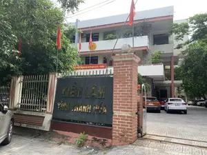 Bức ảnh chụp lối vào của một tòa nhà văn phòng, đây là trụ sở của Chi cục Kiểm lâm tỉnh Thanh Hóa. Trên trụ cổng lớn xây bằng gạch đỏ có một tấm biển màu đen với dòng chữ vàng 'KIỂM LÂM TỈNH THANH HÓA'. Phía trên cổng có treo một băng rôn màu đỏ với nội dung: 'CHÀO MỪNG KỶ NIỆM 51 NĂM NGÀY THÀNH LẬP LỰC LƯỢNG KIỂM LÂM VIỆT NAM (21/5/1973 - 21/5/2024)'. Tòa nhà là một công trình nhiều tầng, trên mặt tiền có gắn biểu tượng của lực lượng Kiểm lâm. Xung quanh và phía trước tòa nhà có cắm nhiều lá cờ đỏ. Trong sân có một số ô tô đang đỗ. Khung cảnh được bao quanh bởi nhiều cây xanh.。（日本語訳）。オフィスビルの入り口を写した写真で、これはタインホア省森林保護局の本部です。赤レンガで造られた大きな門柱には、「KIỂM LÂM TỈNH THANH HÓA」と黄色い文字で書かれた黒い看板があります。門の上には、「ベトナム森林保護部隊設立51周年記念（1973年5月21日～2024年5月21日）を祝う」という内容の赤い横断幕が掲げられています。建物は多層階建てで、正面には森林保護部隊のシンボルが取り付けられています。建物の周りと前には、多くの赤い旗が立てられています。庭には数台の車が駐車しています。風景は多くの緑の木々に囲まれています。