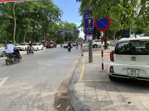 Đây là hình ảnh một con đường phố tại thành phố Thanh Hóa vào một ngày nắng. Trên đường có nhiều phương tiện giao thông như ô tô và xe máy đang di chuyển, và một cô gái đang đi xe đạp. Đèn tín hiệu giao thông đang bật màu xanh. Dọc hai bên đường là vỉa hè và hàng cây xanh. Ở bên phải, một chiếc ô tô màu trắng hiệu KIA Morning đang đỗ trên vỉa hè, bên cạnh một cột có biển báo "Cấm dừng và đỗ xe". Trên đường và trên cột điện có treo các băng rôn và phướn với nội dung:。- Băng rôn vắt ngang đường: "CHÀO MỪNG ĐẠI BIỂU THAM DỰ LIÊN HOAN PHÁT THANH TOÀN QUỐC LẦN THỨ XVI - 2024. Thanh Hóa, ngày 09 - 14/7/2024".。- Phướn treo dọc trên cột: Có logo VOV (Đài Tiếng nói Việt Nam) và nội dung tương tự về "LIÊN HOAN PHÁT THANH TOÀN QUỐC LẦN THỨ XVI - 2024" diễn ra tại Thanh Hóa từ ngày 9-14/7/2024, cùng với logo của các nhà tài trợ như MB Bank và HDBank.。（日本語訳）。これは、晴れた日のタインホア市の街路の写真です。道路上には自動車やバイクなどの多くの交通手段が移動しており、一人の少女が自転車に乗っています。交通信号は青色に点灯しています。道路の両側には歩道と緑の並木があります。右側には、KIAモーニングブランドの白い自動車が、「駐停車禁止」の標識がある柱の隣の歩道に駐車しています。道路上と電柱には、以下の内容の横断幕や垂れ幕が掲げられています。- 道路を横切る横断幕：「第16回全国ラジオフェスティバル2024に参加される代表者の皆様を歓迎します。タインホア、2024年7月9日～14日」。- 柱に縦に掲げられた垂れ幕：VOV（ベトナムの声放送局）のロゴがあり、2024年7月9日から14日までタインホアで開催される「第16回全国ラジオフェスティバル2024」に関する同様の内容、およびMBバンクやHDBankなどのスポンサーのロゴが記載されています。