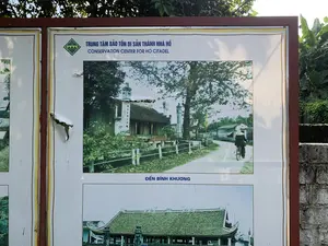 Đây là hình ảnh chụp một tấm biển thông tin lớn đặt ngoài trời, có khả năng là tại khu di tích Thành nhà Hồ. Trên biển có các dòng chữ: "TRUNG TÂM BẢO TỒN DI SẢN THÀNH NHÀ HỒ" và "CONSERVATION CENTER FOR HO CITADEL". Tấm biển trưng bày một số bức ảnh về di tích. Bức ảnh chính ở giữa, có chú thích "ĐỀN BÌNH KHƯƠNG", là một bức ảnh màu cũ mô tả khung cảnh làng quê. Trong ảnh, có một ngôi đền cổ với một tấm bia đá khắc chữ Hán theo chiều dọc ("乘月分明化石魂"). Một người đội nón lá đang đạp xe trên con đường làng. Bên dưới là một bức ảnh khác chụp cận cảnh mái của một công trình kiến trúc cổ. Tấm biển có một vài chỗ bị hư hỏng và rách.。（日本語訳）。これは屋外に設置された大きな案内板を撮影した写真で、おそらく胡朝の城の遺跡区域にあるものです。看板には「TRUNG TÂM BẢO TỒN DI SẢN THÀNH NHÀ HỒ」と「CONSERVATION CENTER FOR HO CITADEL」という文字があります。看板には遺跡に関するいくつかの写真が展示されています。中央の主要な写真には「ĐỀN BÌNH KHƯƠNG」というキャプションがあり、田舎の風景を描写した古いカラー写真です。写真の中には、古い祠と、縦に漢文が刻まれた石碑（「乘月分明化石魂」）があります。菅笠をかぶった人が村の道を自転車で走っています。その下には、古い建築物の屋根を接写した別の写真があります。看板には数か所、損傷したり破れたりしている部分があります。