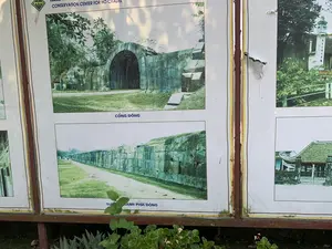 Bức ảnh chụp một tấm bảng thông tin lớn, đã cũ, được đặt ngoài trời tại một khu di tích lịch sử. Trên bảng có nhiều hình ảnh và chú thích liên quan đến Thành nhà Hồ. Phía dưới chân bảng có một vài loại cây nhỏ đang mọc.。Nội dung văn bản có thể đọc được trên bảng bao gồm:。- Logo ở góc trên bên trái có chữ "THÀNH NHÀ HỒ".。- Dòng chữ phía trên: "TRUNG TÂM BẢO TỒN... CONSERVATION CENTER FOR HO CITADEL".。- Chú thích cho bức ảnh lớn ở giữa, phía trên: "CỔNG ĐÔNG". Bức ảnh này cho thấy một cổng thành bằng đá có kiến trúc mái vòm, được xây dựng từ những khối đá lớn, xung quanh là cây cối và bãi cỏ.。- Chú thích cho bức ảnh bên dưới: "TƯỜNG THÀNH PHÍA ĐÔNG". Bức ảnh này chụp một đoạn tường thành dài, thẳng, được xây bằng đá, với một con đường đất chạy dọc theo chân tường.。Ngoài ra, ở phía bên phải có một bức ảnh khác chụp một công trình kiến trúc cổ, có treo một biểu ngữ với dòng chữ Hán "乘月分明化石魂". Tấm bảng thông tin có dấu hiệu bị bong tróc và phần khung kim loại bị gỉ sét.。（日本語訳）。写真には、ある史跡の屋外に設置された、古くなった大きな案内板が写っている。板の上には、胡朝の城に関連する多くの写真と説明書きがある。案内板の足元には、数種類の小さな植物が生えている。案内板で読み取れる文章の内容は以下の通り：。- 左上のロゴには「THÀNH NHÀ HỒ」という文字がある。- 上部の文字列：「TRUNG TÂM BẢO TỒN... CONSERVATION CENTER FOR HO CITADEL」。- 中央上部の大きな写真の説明書き：「CỔNG ĐÔNG」。この写真は、大きな石のブロックで建てられたアーチ構造の石造りの城門を示しており、周りには木々や芝生が広がっている。- 下の写真の説明書き：「TƯỜNG THÀNH PHÍA ĐÔNG」。この写真は、石で造られた長くまっすぐな城壁の一部を写しており、壁の麓に沿って土の道が続いている。案内板には剥がれの兆候があり、金属製のフレーム部分は錆びている。