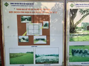 Đây là hình ảnh chụp hai tấm bảng thông tin lớn được đặt ngoài trời, có khả năng là tại một khu di tích. Tấm bảng bên trái có tiêu đề lớn: "TRUNG TÂM BẢO TỒN DI SẢN THÀNH NHÀ HỒ" và dòng chữ tiếng Anh "CONSERVATION CENTER FOR HO CITADEL". Nội dung chính của bảng giới thiệu về "THÀNH NHÀ HỒ VỚI GIÁ TRỊ NỔI BẬT TOÀN CẦU" và việc di sản này "ĐƯỢC UNESCO CÔNG NHẬN DI SẢN THẾ GIỚI VỚI 3 KHU VỰC ĐỀ CỬ". Trên bảng có dán một sơ đồ của "KHU KHAI QUẬT LẦN I" với các chú thích như "CỬA BẮC", "CỬA TÂY", "CỬA ĐÔNG", "CỬA NAM", "Tường thành ốp đá", và "Tường thành đắp đất". Xung quanh sơ đồ là các bức ảnh chụp các cổng thành bằng đá. Phía dưới là các hình ảnh khác được chú thích: "HOÀNG THÀNH", "LA THÀNH" (chụp một cánh đồng lúa xanh), và "ĐÀN NAM GIAO" (chụp một khu vực khai quật khảo cổ). Tấm bảng bên phải cũng có cùng tiêu đề, trưng bày một bức ảnh lớn về một cây cổ thụ bên cạnh một phần của cổng thành và một bức ảnh nhỏ hơn ở dưới về "ĐÔI RỒNG ĐÁ" trên bãi cỏ. Toàn bộ khung cảnh cho thấy đây là một bảng thông tin nhằm giới thiệu cho du khách về lịch sử, cấu trúc và giá trị của khu di tích Thành nhà Hồ.。（日本語訳）。これは屋外に設置された2つの大きな案内板を撮影した写真で、おそらく遺跡にあるものと思われます。左側の案内板には、「TRUNG TÂM BẢO TỒN DI SẢN THÀNH NHÀ HỒ」（胡朝の城塞遺跡保存センター）という大きな見出しと、「CONSERVATION CENTER FOR HO CITADEL」という英語の文字があります。案内板の主な内容は、「THÀNH NHÀ HỒ VỚI GIÁ TRỊ NỔI BẬT TOÀN CẦU」（顕著な普遍的価値を持つ胡朝の城塞）について紹介しており、この遺産が「ĐƯỢC UNESCO CÔNG NHẬN DI SẢN THẾ GIỚI VỚI 3 KHU VỰC ĐỀ CỬ」（推薦された3つの区域でユネスコの世界遺産に認定された）ことを示しています。案内板には、「KHU KHAI QUẬT LẦN I」（第一次発掘区域）の地図が貼られており、「CỬA BẮC」（北門）、「CỬA TÂY」（西門）、「CỬA ĐÔNG」（東門）、「CỬA NAM」（南門）、「Tường thành ốp đá」（石張りの城壁）、「Tường thành đắp đất」（土盛りの城壁）といった注釈が付いています。地図の周りには、石造りの城門を撮影した写真があります。その下には、「HOÀNG THÀNH」（皇城）、「LA THÀNH」（羅城）（青々とした田んぼを撮影したもの）、そして「ĐÀN NAM GIAO」（南郊壇）（考古学的な発掘区域を撮影したもの）と注釈が付けられた他の写真があります。右側の案内板も同じ見出しで、城門の一部と古木の大きな写真、そしてその下には芝生の上にある「ĐÔI RỒNG ĐÁ」（一対の石龍）の小さな写真が展示されています。全体の風景から、これが胡朝の城塞遺跡の歴史、構造、価値を観光客に紹介するための案内板であることがわかります。