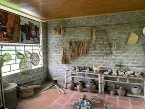 これは屋内の空間で、昔のベトナムの農村の家のように装飾されており、展示室か博物館かもしれません。壁は粗いスラグレンガで建てられ、床には赤いタイルが敷かれています。壁には、乾燥した稲穂、乾燥したトウモロコシ、馬鍬、藁箒、古い竿秤といった農具や生活用品が掛けられています。2つの竹製の棚には、様々な種類の碗、皿、壺などの陶磁器が多数展示されています。床の上にも、土製の大きな壺や甕が多数置かれています。部屋の隅には、鋳鉄の鍋が三脚の五徳の上に置かれた薪のかまどが再現されています。床の上にはさらに、食事やお茶会の光景を思わせるように、茶器一式と碗や皿が並べられています。窓の近くには、竹で編まれた様々な種類の籠やざるが掛けられています。窓の上には、陶器作りと料理の場面を描いた大きな絵があります