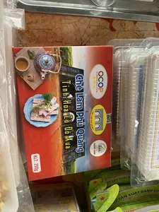 Hình ảnh chụp cận cảnh một hộp đặc sản Chè Lam Phủ Quảng đang được trưng bày, có thể là tại một cửa hàng hoặc quầy hàng. Trên vỏ hộp màu đỏ có ghi các thông tin: 'Chè Lam Phủ Quảng', 'Tinh Hoa Cổ Đô Xưa', và 'KLT: 250g'. Hộp có logo chứng nhận sản phẩm OCOP 3 sao ('ONE COMMUNE ONE PRODUCT OF VIETNAM') và logo của cơ sở sản xuất 'BÁNH KẸO CƯƠNG XUÂN'. Hình ảnh trên bao bì mô tả món chè lam đã được cắt lát, đặt trên đĩa xanh cùng với một bộ ấm chén trà hoa văn truyền thống. Phía sau là hình ảnh một công trình kiến trúc cổ bằng đá, có thể là cổng thành. Xung quanh hộp chè lam là các sản phẩm được đóng gói khác, cho thấy đây là một nơi bán hàng.。（日本語訳）。フー・クアンの特産品「チェー・ラム」の箱が、おそらく店か屋台で展示されているクローズアップ写真。赤い箱には、「Chè Lam Phủ Quảng（フー・クアンのチェー・ラム）」、「Tinh Hoa Cổ Đô Xưa（古都の精華）」、そして「KLT: 250g（正味重量：250g）」という情報が記載されている。箱には、OCOP三つ星製品認証ロゴ（「ONE COMMUNE ONE PRODUCT OF VIETNAM」）と、製造元「BÁNH KẸO CƯƠNG XUÂN（クオン・スアン製菓）」のロゴがある。背景には、おそらく城門と思われる石造りの古い建築物の画像がある。チェー・ラムの箱の周りには他の包装された製品があり、ここが販売場所であることを示している。