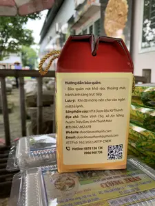 Bức ảnh chụp cận cảnh bao bì sản phẩm được đặt ngoài trời, có thể tại một cửa hàng hoặc quầy hàng. Đối tượng chính là một hộp giấy màu vàng và đỏ có quai xách.。Trên nhãn của hộp giấy có ghi các thông tin sau:。- Hướng dẫn bảo quản: Bảo quản nơi khô ráo, thoáng mát, tránh ánh sáng trực tiếp.。- Lưu ý: Khi đã mở lọ nên cho vào ngăn mát tủ lạnh.。- Sản phẩm của: HTX Dược liệu Xứ Thanh。- Địa chỉ: Thôn Vĩnh Thọ, xã An Nông, huyện Triệu Sơn, tỉnh Thanh Hóa。- ĐT: 0947.862.678。- Website: duoclieuxuthanh.com。- Email: duoclieuxuthanh@gmail.com。- ATTP số: 162/2022/ATTP-CNĐK。- Hotline: 0878 136 136, 0966 968 736。- Có một mã QR.。Bên dưới hộp giấy là các hộp nhựa trong suốt đựng sản phẩm khác, có thể là bánh kẹo. Trên nhãn của các hộp này có các dòng chữ:。- 'Đặc sản Xứ Thanh', 'Thơm Ngon Tinh khiết'.。- 'CƠ SỞ SẢN XUẤT BÁNH KẸO GIA TRUYỀN CƯƠNG XUÂN', địa chỉ tại 'Khu phố Nhân Lộ - TT.Vĩnh Lộc - Thanh Hóa' và số điện thoại '0859 290 798'.。- Thành phần: 'Nếp cái Hoa vàng, mật mía, lạc, mạch nha, hương liệu gia truyền...'.。- 'HSD: 90 ngày - NSX:'.。Khung cảnh nền bị làm mờ, cho thấy cây cối, nhà cửa và một người đang đội nón lá ở phía xa. Hoạt động chính trong ảnh là trưng bày các sản phẩm đặc sản địa phương.。（日本語訳）。屋外、おそらく店か屋台に置かれた製品パッケージのクローズアップ写真です。主な被写体は、持ち手付きの黄色と赤色の紙箱です。紙箱のラベルには、以下の情報が記載されています。- 保存方法：乾燥した涼しい場所で保管し、直射日光を避けてください。- 注意：瓶を開封後は、冷蔵庫のチルド室に入れてください。- 製造元：スータイン薬草協同組合。- 住所：タインホア省、トリウソン県、アンノン社、ヴィントー村。- 電話番号：0947.862.678。- ウェブサイト：duoclieuxuthanh.com。- Eメール：duoclieuxuthanh@gmail.com。- 食品安全衛生登録証明書番号：162/2022/ATTP-CNĐK。- ホットライン：0878 136 136, 0966 968 736。- QRコードが1つあります。紙箱の下には、他のおそらくお菓子と思われる製品が入った透明なプラスチックの箱があります。これらの箱のラベルには、以下の文言が記載されています。- 「スータイン特産品」、「香り高く、美味しく、純粋」。- 「クオン・スアン家伝菓子製造所」、住所「タインホア省、ヴィンロック町、ニャンロー街区」、電話番号「0859 290 798」。- 原材料：「ネップカイホアヴァン（もち米）、サトウキビ糖蜜、落花生、麦芽糖、家伝の香料...」。- 「賞味期限：90日間 - 製造年月日：」。背景はぼかされており、木々、家々、そして遠くにノンラー（ベトナムの伝統的な笠）をかぶった一人の人物が見えます。写真の中の主な活動は、地元の特産品を陳列することです。