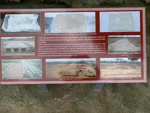 Đây là một bảng thông tin được đặt tại một khu di tích khảo cổ, có thể là Thành Nhà Hồ dựa trên nội dung. Bảng có nền màu đỏ sẫm, chữ trắng, và viền trang trí hoa văn. Bảng cung cấp thông tin về các cuộc khai quật khảo cổ học và trưng bày hình ảnh về các di tích, hiện vật được tìm thấy.。**Nội dung văn bản được ghi trên bảng:**。[Tiêu đề phụ] Hệ thống chân tảng: từ kinh thành Thăng Long và sản xuất tại địa phương。[Đoạn văn chính]。Cuộc khai quật khảo cổ học trong khu vực Nội thành Thành Nhà Hồ đã minh chứng cho những ghi chép trong sử sách về những cung điện, đền đài trong thành nội là hoàn toàn trùng khớp.。Đây là những chân tảng được phát hiện qua khai quật tại một số vị trí kiến trúc quan trọng trong Nội thành: con đường Hoàng Gia, khu vực Chính điện (nơi Vua thiết triều), khu vực kiến trúc phía Đông (Đông Thái Miếu), khu kiến trúc phía Tây (Tây Thái Miếu), nơi sinh hoạt của Hoàng gia (tẩm điện). Có hai loại hiện vật kiến trúc theo xuất xứ. Một loại từ phá bỏ các cung điện ở kinh thành Thăng Long mang vào, một loại sản xuất tại chỗ. Chân tảng ở đây cũng vậy, đúng như những điều sử sách đã ghi chép.。[Chú thích các hình ảnh]。- Cống thoát nước。- Sân lát đá。- Khu vực nền Vua。- Toàn cảnh khai quật trong Nội thành。- gạch và móng trụ khu vực Đông Thái Miếu。**Mô tả các hình ảnh trên bảng:**。- **Địa điểm:** Các hình ảnh mô tả một khu vực khai quật khảo cổ ngoài trời, cụ thể là tại Nội thành Thành Nhà Hồ.。- **Hoạt động:** Một bức ảnh cho thấy các nhà khảo cổ học đang làm việc tại hiện trường khai quật. Họ đang đào và nghiên cứu các di tích.。- **Vật thể:** Các bức ảnh khác chụp cận cảnh các phát hiện khảo cổ, bao gồm: các chân tảng bằng đá (một số có điêu khắc hoa văn), một hệ thống cống thoát nước bằng đá, một khoảng sân được lát đá, nền móng của một công trình được xây bằng gạch và đá, và một khu vực được gọi là 'nền Vua'.。（日本語訳）。これは考古学遺跡に設置された案内板で、内容から胡朝の城塞である可能性があります。案内板は濃い赤色の背景に白い文字で、装飾的な模様の縁取りがあります。この案内板は、考古学的発掘調査に関する情報を提供し、発見された遺跡や遺物の写真を展示しています。**案内板に記載されている文章の内容：**。[副題] 礎石システム：タンロン城からのものと現地で生産されたもの。[本文]。胡朝の城塞の内城区域における考古学的発掘調査は、内城内の宮殿や祠堂に関する史書の記述が完全に一致することを証明しました。これらは、内城内のいくつかの重要な建築場所での発掘調査によって発見された礎石です：王道、正殿区域（王が政務を執った場所）、東側建築区域（東太廟）、西側建築区域（西太廟）、王家の生活の場（寝殿）。出所によって2種類の建築遺物があります。1つはタンロン城の宮殿を取り壊して持ち込まれたもの、もう1つは現地で生産されたものです。ここの礎石も同様で、史書に記されている通りです。[写真のキャプション]。- 排水溝。- 石畳の中庭。- 王の基壇区域。- 内城内の発掘全景。- 東太廟区域のレンガと柱の基礎。**案内板上の写真の説明：**。- **場所：** 写真は屋外の考古学発掘区域、具体的には胡朝の城塞の内城を描写しています。彼らは遺跡を掘り、研究しています。- **物体：** 他の写真は、石の礎石（一部には模様が彫刻されている）、石造りの排水溝システム、石畳の中庭、レンガと石で造られた建造物の基礎、そして「王の基壇」と呼ばれる区域を含む、考古学的発見物のクローズアップです。