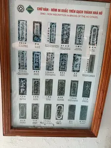 Bức ảnh chụp một tấm bảng thông tin được đóng trong khung gỗ, có khả năng được trưng bày tại một bảo tàng hoặc khu di tích. Tiêu đề của bảng là "CHỮ HÁN - NÔM IN KHẮC TRÊN GẠCH THÀNH NHÀ HỒ", với phụ đề tiếng Anh "SINO - NOM INSCRIPTION IN BRICKS OF THE HO CITADEL". Trên bảng có hai logo ở góc trên bên trái, một trong số đó là logo Di sản Thế giới của UNESCO. Nội dung chính của bảng là tập hợp hình ảnh các viên gạch cổ có khắc chữ Hán-Nôm. Mỗi hình ảnh đi kèm với chú thích bao gồm chữ gốc, phiên âm và tên địa danh hiện đại. Đây là các địa danh đã đóng góp vào việc xây dựng Thành nhà Hồ. Các dòng chữ được ghi lại bao gồm:。Hàng 1: An Tôn Thượng xã, Bái xã, Du Mạng Nê xã, Cảo phường, Hoàng Tranh [Xá] xã, Cá Nưa Hạ, La Hắc xã.。Hàng 2: Mạng Nê xã Cải phường, Như Lai xã, Cổ Lỗi huyện, Trà Lị xã, Đào Xá xã, Mộc Bất, Đông Sơn huyện, Lê Nguyễn Xá xã.。Hàng 3: Đặc Tượng xã, Đại Tiền xã, Cá Nưa xã, An Định huyện..., Tiểu Phúc Lâm phường, Thượng Hộ xã.。Hàng 4: Diên Thạch xã, Chân Lị xã, Vĩnh Ninh, Đầu Trại xã, Vương Triền, Hồng Hỏa, Di Thử/Hỏa.。（日本語訳）。写真は木製のフレームに収められた案内板を写したもので、博物館または史跡に展示されている可能性があります。案内板のタイトルは「胡朝の城の煉瓦に刻まれた漢字・ノム文字」で、英語のサブタイトルは「SINO - NOM INSCRIPTION IN BRICKS OF THE HO CITADEL」です。案内板の左上隅には2つのロゴがあり、そのうちの1つはユネスコ世界遺産のロゴです。案内板の主な内容は、漢字・ノム文字が刻まれた古代の煉瓦の写真を集めたものです。各写真には、元の文字、翻字、現代の地名を含む注釈が付いています。これらは胡朝の城の建設に貢献した地名です。記録されている文字列は以下の通りです。1行目：アントン・トゥオン社、バイ社、ズー・マン・ネー社、カオ坊、ホアン・チャイン［サー］社、カー・ヌア・ハ、ラ・ハック社。2行目：マン・ネー社カイ坊、ニュー・ライ社、コー・ロイ県、チャー・リー社、ダオ・サー社、モック・バット、ドン・ソン県、レ・グエン・サー社。3行目：ダック・トゥオン社、ダイ・ティエン社、カー・ヌア社、アン・ディン県…、ティエウ・フック・ラム坊、トゥオン・ホー社。4行目：ジエン・タック社、チャン・リー社、ヴィン・ニン、ダウ・チャイ社、ヴオン・チエン、ホン・ホア、ジー・トゥー／ホア。