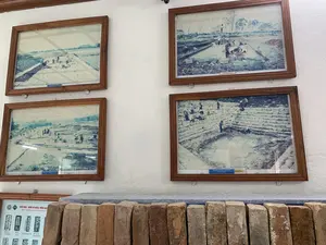 Bên trong một không gian trưng bày, có thể là bảo tàng hoặc khu di tích, trên một bức tường trắng có treo bốn bức ảnh tư liệu được lồng khung gỗ. Phía dưới các bức ảnh, trên một bệ đá, là một hàng gạch cổ được trưng bày. Các bức ảnh tư liệu mô tả các hoạt động tại một công trường khảo cổ học, cho thấy nhiều người đang tham gia vào công việc khai quật, đào đất, và bảo tồn các công trình kiến trúc bằng đá. Một số người lao động đội nón lá. Ở góc dưới bên trái, có một tấm áp phích giới thiệu về các chữ Hán - Nôm được in khắc trên gạch.。Các dòng chữ được ghi lại bao gồm:。- Chú thích dưới các bức ảnh: "Khai quật Thành Nhà Hồ (2010)", "Khai quật Di tích Đàn tế Nam Giao (2010)", và "Bảo tồn Di tích Giếng Vua tại Đàn tế Nam Giao (2010)".。- Trên tấm áp phích ở góc dưới bên trái có tiêu đề: "CHỮ HÁN - NÔM IN KHẮC TRÊN GẠCH" và dòng chữ tiếng Anh "SINO-NOM INSCRIPTION IN BRICKS OF...". Tấm áp phích này minh họa các ký tự trên gạch như "安孫上社" (An Tôn Thượng xã), "黃華會位" (Hoàng Hoá Hội Vị), và "多忙把社平坊" (Đa Mang Ba xã Bình phường).。（日本語訳）。展示空間の中、それは博物館か遺跡地区かもしれないが、白い壁に木製の額縁に入れられた4枚の資料写真が掛けられている。写真の下、石の台座の上には、古代のレンガが一列に展示されている。資料写真は考古学の発掘現場での活動を描写しており、多くの人々が発掘、土掘り、石造りの建築物の保存作業に参加している様子が写っている。一部の労働者はノンラー（菅笠）をかぶっている。左下の隅には、レンガに印刻された漢字・チュノムを紹介するポスターがある。記録されている文字には以下が含まれる：。- 写真の下のキャプション：「胡朝の城塞の発掘（2010年）」、「南郊壇遺跡の発掘（2010年）」、そして「南郊壇の王の井戸遺跡の保存（2010年）」。- 左下の隅のポスターには、「レンガに印刻された漢字・チュノム」という見出しと、「SINO-NOM INSCRIPTION IN BRICKS OF...」という英語の文字列がある。このポスターは、「安孫上社」（An Tôn Thượng xã）、「黃華會位」（Hoàng Hoá Hội Vị）、そして「多忙把社平坊」（Đa Mang Ba xã Bình phường）のようなレンガ上の文字を図解している。