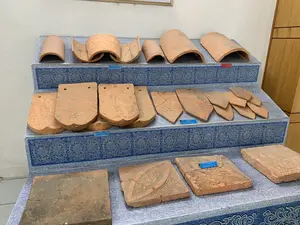 Hình ảnh chụp tại một bảo tàng hoặc phòng trưng bày, nơi các hiện vật khảo cổ được trưng bày trên một kệ nhiều tầng. Kệ được phủ bằng một lớp giấy hoặc vải có hoa văn màu xanh dương và trắng. Các hiện vật là các loại gạch và ngói bằng đất nung cổ, có niên đại từ nhiều thế kỷ trước. Có các biển chú thích nhỏ màu xanh cung cấp thông tin về các hiện vật.。Nội dung các biển chú thích có thể đọc được:。1. "NGÓI ÂM DƯƠNG, THẾ KỶ 14 - 15": Dành cho bộ ngói cong ở tầng trên cùng.。2. "NGÓI MŨI SEN, THẾ KỶ 14 - 15": Dành cho các viên ngói phẳng, đầu tròn ở tầng giữa.。3. "Ngói mũi lá, Đất nung, triều Trần - Hồ, thế kỷ 14 - 15": Dành cho các viên ngói phẳng, đầu nhọn ở tầng giữa.。4. "GẠCH LÁT NỀN TRANG TRÍ HOA CHANH (Gạch hoa chanh), Đất nung, triều Trần - Hồ, thế kỷ 14 - 15": Dành cho các viên gạch lát nền hình vuông có hoa văn nổi ở tầng dưới cùng.。Hoạt động chính là trưng bày các vật liệu xây dựng kiến trúc cổ của Việt Nam, cho thấy các kỹ thuật và kiểu dáng khác nhau của gạch và ngói qua các thời kỳ lịch sử.。（日本語訳）。ある博物館または展示室で撮影された写真で、考古学的遺物が多層の棚に展示されています。棚は青と白の模様がある紙または布で覆われています。遺物は古代のテラコッタ製の様々な種類のレンガと瓦で、数世紀前のものです。遺物に関する情報を提供する小さな青いキャプションプレートがあります。読み取れるキャプションプレートの内容：。1. 「陰陽瓦、14～15世紀」：最上段にある湾曲した瓦セット用。2. 「蓮頭瓦、14～15世紀」：中段にある、先端が丸い平瓦用。3. 「葉頭瓦、テラコッタ、陳・胡朝、14～15世紀」：中段にある、先端が尖った平瓦用。4. 「柑橘花装飾床レンガ（柑橘花レンガ）、テラコッタ、陳・胡朝、14～15世紀」：最下段にある、浮き彫り模様の四角い床用レンガ用。主な活動はベトナムの古代建築の建材を展示することであり、歴史的な各時代におけるレンガと瓦の様々な技術と様式を示しています。