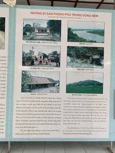 Bức ảnh chụp một tấm bảng thông tin được trưng bày, có thể ở một bảo tàng hoặc trung tâm du khách, giới thiệu về các di sản trong vùng đệm của Di sản Thành Nhà Hồ. Tấm bảng được trình bày song ngữ Việt - Anh.。Nội dung văn bản được ghi lại như sau:。Tiêu đề: 'NHỮNG DI SẢN PHONG PHÚ TRONG VÙNG ĐỆM' và 'DIVERSE HERITAGE IN THE BUFFER ZONE'.。Bảng thông tin có sáu hình ảnh kèm chú thích:。- 'ĐÈN TRẦN KHÁT CHÂN - TRAN KHAT CHAN TEMPLE': Hình ảnh một ngôi đền có sân rộng phía trước.。- 'SÔNG MÃ - MA RIVER': Hình ảnh một con sông rộng lớn với bờ bên kia là đồng bằng xanh.。- 'CHÙA TƯỜNG VÂN - TUONG VAN PAGODA': Hình ảnh cổng vào của một ngôi chùa với kiến trúc truyền thống.。- 'HANG NÀNG - NANG CAVE': Hình ảnh một hang đá nhỏ, tự nhiên.。- 'NHÀ CỔ - ANCIENT HOUSE': Hình ảnh một ngôi nhà cổ lợp ngói âm dương với hàng cột gỗ.。- 'NÚI THỔ TƯỢNG - THO TUONG MOUNTAIN': Hình ảnh một ngọn núi cây cối rậm rạp, phía trước là một cánh đồng lúa xanh.。Phần văn bản mô tả bằng tiếng Việt: 'Giá trị của Di sản Thành Nhà Hồ không chỉ ở những công trình kiến trúc thành quách, cung điện trong vùng bảo vệ mà còn được tôn lên gấp nhiều lần bởi những di sản thiên nhiên, di sản văn hóa vật thể và phi vật thể đa dạng và độc đáo trong vùng đệm. Chúng trực tiếp hoặc gián tiếp kể cho ta nghe những câu chuyện liên quan tới tòa thành lịch sử. Đó là núi An Tôn, núi Tiến Sỹ, núi Thổ Tượng, núi Hắc Khuyển, núi Ngọa Ngưu, sông Bưởi, sông Mã, động Hồ Công, đền thờ nàng Bình Khương, đền thờ Trần Khát Chân, đình Đông Môn, đình Tây Giai và các nhà cổ dân gian v.v... Tất cả tô đậm thêm những sự kiện lịch sử thời Hồ và những giá trị của Di sản Thế giới Thành Nhà Hồ.'。（日本語訳）。展示されている案内板を撮影した写真で、おそらく博物館かビジターセンターにあり、胡朝の城の遺産の緩衝地帯にある遺産を紹介しています。案内板はベトナム語と英語のバイリンガルで表示されています。記載されているテキストの内容は以下の通りです。タイトル：「緩衝地帯における豊かな遺産」および「DIVERSE HERITAGE IN THE BUFFER ZONE」。案内板には6枚の写真とキャプションが付いています。- 「チャン・カット・チャン祠 - TRAN KHAT CHAN TEMPLE」：前に広い庭がある祠の写真。- 「マー川 - MA RIVER」：対岸に緑の平野が広がる大きな川の写真。- 「トゥオンヴァン寺 - TUONG VAN PAGODA」：伝統的な建築様式の寺院の入り口の門の写真。- 「ナン洞窟 - NANG CAVE」：小さな自然の洞窟の写真。- 「古民家 - ANCIENT HOUSE」：陰陽瓦で葺かれ、木の柱が並ぶ古民家の写真。- 「トートゥオン山 - THO TUONG MOUNTAIN」：木々が鬱蒼と茂る山で、その手前には緑の田んぼが広がる写真。ベトナム語による説明文：「胡朝の城の遺産の価値は、保護区域内の城郭や宮殿といった建築物にあるだけでなく、緩衝地帯にある多様で独特な自然遺産、有形・無形の文化遺産によって何倍にも高められています。それらは、直接的または間接的に、この歴史的な城に関連する物語を私たちに語りかけます。それは、アントン山、ティエンシー山、トートゥオン山、ハックエン山、ゴアグウ山、ブオイ川、マー川、ホーコン洞窟、ビンクオン妃祠、チャン・カット・チャン祠、ドンモン亭、タイザイ亭、そして民間の古民家などです。全てが、胡朝時代の歴史的な出来事と、世界遺産である胡朝の城の価値をさらに際立たせています。」