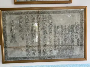 Bức ảnh chụp một bản dập văn bia đá (thác bản) được lồng trong một khung gỗ màu vàng và treo trên tường trắng. Đây là một hiện vật được trưng bày trong nhà, có thể tại một khu di tích lịch sử hoặc bảo tàng.。**Mô tả chi tiết:**。*   **Địa điểm:** Không gian trong nhà, có khả năng là một phòng trưng bày tại khu di tích Động Hồ Công, Thanh Hóa, hoặc một bảo tàng liên quan.。*   **Vật thể:** Đối tượng chính là một bản dập từ bia đá cổ, có các ký tự chữ Hán được khắc nổi. Bản dập có màu xám đen, được đặt trong khung gỗ màu vàng có mặt kính bảo vệ. Xung quanh phần chữ viết có một đường diềm trang trí hoa văn phức tạp. Phía dưới khung ảnh có một dải hoa văn trang trí tường màu xanh nhạt.。*   **Hoạt động:** Bức ảnh ghi lại việc trưng bày và bảo tồn một di sản văn hóa, không có hoạt động của con người diễn ra.。**Nội dung văn tự (chữ Hán):**。Đây là bản dập bài thơ "Đề Hồ Công Động" của vua Lê Thánh Tông. Văn bản được viết theo cột dọc, đọc từ phải sang trái. Nội dung chính có thể phiên âm Hán-Việt như sau:。*   **Tiêu đề (phảiสุด):** 題壺公洞并引 (Đề Hồ Công Động tịnh dẫn)。*   **Lời dẫn:** 洪德九年仲春戊子... (Hồng Đức cửu niên Trọng xuân Mậu Tý... - Năm Hồng Đức thứ 9, tháng hai, ngày Mậu Tý...)。*   **Nội dung bài thơ:**。神椎鬼鑿萬重山 (Thần chùy quỷ tạc vạn trùng san)。虛室寥寥宇宙寬 (Hư thất liêu liêu vũ trụ khoan)。世上功名都是夢 (Thế thượng công danh đô thị mộng)。洞中日月不勝閑 (Động trung nhật nguyệt bất thắng nhàn)。龍化去珠隊碧落 (Long hóa khứ châu đội bích lạc)。泉流白玉寒 (Tuyền lưu bạch ngọc hàn)。我欲乘風凌絕頂 (Ngã dục thừa phong lăng tuyệt đỉnh)。望窮雲海有無間 (Vọng cùng vân hải hữu vô gian)。*   **Bút danh (tráiสุด):** 天南洞主題 (Thiên Nam động chủ đề - Bút danh của vua Lê Thánh Tông)。（日本語訳）。黄色い木製の額縁に入れられ、白い壁に掛けられた石碑の拓本（thác bản）を写した写真です。これは屋内で展示されている現物で、歴史的遺跡または博物館にある可能性があります。**詳細な説明：**。*   **場所：** 屋内空間。タインホア省のホーコン洞窟遺跡の展示室、または関連する博物館である可能性があります。*   **物体：** 主な対象は、漢字が浮き彫りにされた古い石碑の拓本です。拓本は黒灰色で、保護ガラス付きの黄色い木製の額縁に収められています。文字部分の周りには、複雑な模様の装飾的な縁取りがあります。額縁の下には、薄い青色の壁の装飾模様の帯があります。*   **活動：** この写真は文化遺産の展示と保存を記録したものであり、人間の活動は行われていません。**文字の内容（漢字）：**。これは黎聖宗（レ・タイントン）王の詩「題壺公洞（Đề Hồ Công Động）」の拓本です。文章は縦書きで、右から左に読みます。主な内容は、以下のように漢越語で音写できます。*   **題名（一番右）：** 題壺公洞并引（Đề Hồ Công Động tịnh dẫn）。*   **序文：** 洪德九年仲春戊子...（Hồng Đức cửu niên Trọng xuân Mậu Tý... - 洪德9年、2月、戊子の日...）。*   **詩の内容：**。神椎鬼鑿萬重山（Thần chùy quỷ tạc vạn trùng san）。虛室寥寥宇宙寬（Hư thất liêu liêu vũ trụ khoan）。世上功名都是夢（Thế thượng công danh đô thị mộng）。洞中日月不勝閑（Động trung nhật nguyệt bất thắng nhàn）。龍化去珠隊碧落（Long hóa khứ châu đội bích lạc）。泉流白玉寒（Tuyền lưu bạch ngọc hàn）。我欲乘風凌絕頂（Ngã dục thừa phong lăng tuyệt đỉnh）。望窮雲海有無間（Vọng cùng vân hải hữu vô gian）。*   **筆名（一番左）：** 天南洞主題（Thiên Nam động chủ đề - 黎聖宗王の筆名）