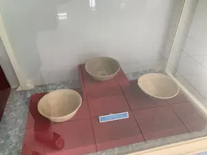 Trong ảnh là ba chiếc bát gốm cổ được trưng bày bên trong một tủ kính tại một bảo tàng hoặc phòng trưng bày. Các chiếc bát có màu be hoặc trắng ngà, được đặt trên một bệ trưng bày màu đỏ. Ở giữa có một tấm biển nhỏ ghi chú thích bằng tiếng Việt và tiếng Anh. Dòng chữ tiếng Việt là: 'Bát men, gốm thế kỷ 14 - 15'. Hoạt động chính là trưng bày hiện vật lịch sử. Các vật thể trong ảnh bao gồm bát gốm, tủ kính và bảng chú thích.。（日本語訳）。碗はベージュ色または象牙色で、赤い展示台の上に置かれています。中央にはベトナム語と英語で注釈が書かれた小さな札があります。ベトナム語の表記は「釉薬碗、14～15世紀の陶器」です。主な活動は歴史的遺物の展示です。写真に写っている物には、陶磁器の碗、ガラスケース、注釈の札が含まれます。