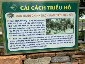Bức ảnh chụp một tấm biển thông tin lịch sử đặt ngoài trời tại khu di tích Thành nhà Hồ, Thanh Hóa. Tấm biển có nền màu xanh lá cây, chữ màu vàng và trắng, được đặt trên một bức tường xây bằng đá và gạch cũ. Biển cung cấp thông tin về các cải cách dưới triều đại nhà Hồ.。Nội dung văn bản trên biển như sau:。[Logo] THE HO CITADEL - THÀNH NHÀ HỒ - DI SẢN VĂN HÓA THẾ GIỚI。[Tiêu đề chính] CẢI CÁCH TRIỀU HỒ。[Tiêu đề phụ] BAN HÀNH CHÍNH SÁCH HẠN ĐIỀN, HẠN NÔ。[Nội dung chi tiết]。'Năm 1397, Hồ Quý Ly đặt ra phép hạn điền, tức là hạn chế việc sở hữu ruộng tư. Nhà nước tiến hành đo đạc lại ruộng đất, diện tích thừa phải sung công. Chính sách này đã giúp cho người nông dân được làm chủ, canh tác, sản xuất trên chính mảnh đất của mình, thúc đẩy sự phát triển nền kinh tế.。Năm 1401, nhà Hồ ban hành phép hạn nô, các quý tộc bị hạn chế số nô tì, giải phóng một lượng nô bộc lúc bấy giờ. Chính sách hạn điền, hạn nô đã có những tác động đến đời sống của tầng lớp nhân dân, làm thay đổi tình hình kinh tế và chính trị xã hội khi ấy. Đây cũng là một trong những cải cách được các triều đại về sau áp dụng và phổ biến trong việc xây dựng đất nước.'。Bên cạnh phần chữ là một bức ảnh tư liệu đen trắng, mô tả một nhóm người trong trang phục truyền thống thời xưa, một số người đội nón lá, đang tham gia một hoạt động cộng đồng hoặc một đám rước.。（日本語訳）。タインホア省、胡朝の城跡の屋外に設置された歴史情報案内板を写した写真。案内板は胡朝時代の改革に関する情報を提供している。案内板の文面は以下の通りです。[ロゴ] THE HO CITADEL - 胡朝の城 - 世界文化遺産。[主な見出し] 胡朝の改革。[副見出し] 限田・限奴政策の公布。[詳細内容]。「1397年、胡季犛は限田法、すなわち私有田の所有を制限する法律を制定した。国家は田畑を再測量し、超過した面積は公収しなければならなかった。この政策は、農民が自らの土地の主となり、耕作し、生産することを助け、経済の発展を促進した。1401年、胡朝は限奴法を公布し、貴族は奴婢の数を制限され、当時の奴僕の一部が解放された。限田・限奴政策は人民階層の生活に影響を与え、当時の経済および社会政治状況を変化させた。これはまた、後の王朝が国造りにおいて適用し、普及させた改革の一つでもある。」。文字部分の横には、昔の伝統的な衣装を着た人々の集団を描写した白黒の資料写真がある。何人かはノンラー（円錐形の葉笠）をかぶり、地域活動または行列に参加している様子である。