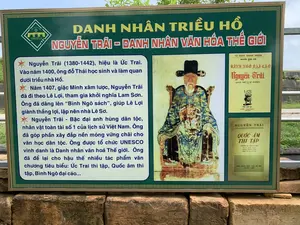 Đây là hình ảnh một tấm bảng thông tin lớn được đặt ngoài trời tại khu di tích Thành nhà Hồ. Tấm bảng có khung màu vàng, nền màu xanh lá cây và được đặt trên một bệ xây bằng gạch đá cũ. Nội dung trên bảng nhằm cung cấp thông tin lịch sử cho du khách về danh nhân Nguyễn Trãi.。Nội dung văn bản được ghi trên bảng như sau:。Logo: "THE HO CITADEL / THÀNH NHÀ HỒ / DI SẢN VĂN HÓA THẾ GIỚI"。Tiêu đề: "DANH NHÂN TRIỀU HỒ / NGUYỄN TRÃI - DANH NHÂN VĂN HÓA THẾ GIỚI"。Nội dung chính:。"* Nguyễn Trãi (1380-1442), hiệu là Ức Trai. Vào năm 1400, ông đỗ Thái học sinh và làm quan dưới triều nhà Hồ.。* Năm 1407, giặc Minh xâm lược, Nguyễn Trãi đã đi theo Lê Lợi, tham gia khởi nghĩa Lam Sơn. Ông đã dâng lên “Bình Ngô sách”, giúp Lê Lợi giành thắng lợi, lập nên nhà Lê Sơ.。* Nguyễn Trãi - Bậc đại anh hùng dân tộc, nhân vật toàn tài số 1 của lịch sử Việt Nam. Ông đã góp phần xây đắp nền móng vững chãi cho văn học dân tộc. Ông được tổ chức UNESCO vinh danh là Danh nhân văn hoá Thế giới. Ông đã để lại cho hậu thế nhiều tác phẩm văn chương tiêu biểu: Ức Trai thi tập, Quốc âm thi tập, Bình Ngô đại cáo..."。Ngoài ra, trên bảng còn có một bức chân dung của Nguyễn Trãi và hình ảnh bìa của hai cuốn sách:。1. "TỦ SÁCH DANH NHÂN / NGUYỄN - NGỌC - KIM / BÌNH NGÔ ĐẠI CÁO / Nguyễn Trãi (THÂN THẾ VÀ SỰ NGHIỆP) / Nhà xuất bản ANH PHƯƠNG HANOI"。2. "NGUYỄN TRÃI / QUỐC ÂM THI TẬP / (TRONG ỨC TRAI DI TẬP) TRẦN VĂN GIÁP PHẠM TRỌNG ĐIỀM PHIÊN ÂM VÀ CHÚ GIẢI / NHÀ XUẤT BẢN VĂN SỬ ĐỊA HÀ NỘI - 1956"。Không có hoạt động nào của con người được ghi lại trong ảnh, chỉ có tấm bảng thông tin lịch sử.。（日本語訳）。これは、胡朝の城跡に屋外設置された大きな案内板の写真です。案内板は黄色の枠、緑色の背景で、古いレンガと石で造られた台座の上に設置されています。板に書かれた内容は、グエン・チャイという偉人に関する歴史情報を観光客に提供することを目的としています。板に記載されている文章の内容は以下の通りです。ロゴ：「THE HO CITADEL / 胡朝の城 / 世界文化遺産」。タイトル：「胡朝の偉人 / グエン・チャイ - 世界文化偉人」。主な内容：。「* グエン・チャイ（1380-1442）、号はウック・チャイ。1400年、彼は科挙の太学生に合格し、胡朝の下で官吏を務めました。* 1407年、明の侵略軍が侵攻すると、グエン・チャイはレ・ロイに従い、ラムソン蜂起に参加しました。彼は「平呉策」を献上し、レ・ロイが勝利を収め、黎前期を建国するのを助けました。* グエン・チャイ - 民族の偉大な英雄であり、ベトナム史上最高の万能の人物。彼は民族文学の強固な基盤を築くことに貢献しました。彼はユネスコによって世界文化偉人として顕彰されました。彼は後世に多くの代表的な文学作品を残しました：『ウック・チャイ詩集』、『国音詩集』、『平呉大誥』など...」。さらに、板にはグエン・チャイの肖像画と2冊の本の表紙の画像があります。1. 「偉人叢書 / グエン - ゴック - キム / 平呉大誥 / グエン・チャイ（その出自と事業） / ANH PHUONG HANOI出版社」。2. 「グエン・チャイ / 国音詩集 / （『ウック・チャイ遺集』より）チャン・ヴァン・ザップ、ファム・チョン・ディエムによる翻音と注解 / 文史地出版社 ハノイ - 1956年」。