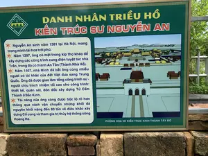 Bức ảnh chụp một bảng thông tin đặt ngoài trời tại khu di tích lịch sử Thành Nhà Hồ. Bảng có khung màu vàng, nền xanh lá cây, được đặt trên một bệ xây bằng gạch đá cổ. Phía sau là cây cối xanh tươi. Nội dung trên bảng giới thiệu về kiến trúc sư Nguyễn An, một danh nhân thời nhà Hồ. Toàn bộ văn bản trên bảng được ghi lại như sau:。Phía trên cùng có logo với dòng chữ "THE HO CITADEL", "THÀNH NHÀ HỒ", và "DI SẢN VĂN HÓA THẾ GIỚI".。Tiêu đề chính: "DANH NHÂN TRIỀU HỒ - KIẾN TRÚC SƯ NGUYỄN AN".。Nội dung chi tiết:。"Nguyễn An sinh năm 1381 tại Hà Nội, mang trong mình tài hoa trời phú.。Năm 1397, ông có mặt trong kíp thợ khéo để xây dựng các công trình cung điện tuyệt tác nhà Trần, trong đó có thành An Tôn (Thành Nhà Hồ).。Năm 1407, nhà Minh đã bắt ông cùng nhiều người có tài khác của đất Việt đưa sang Trung Quốc. Ông đã được giao làm tổng công trình sư - người chịu trách nhiệm tối cao cho công trình: thiết kế, quán sát, đôn đốc xây dựng Tử Cấm Thành ở Bắc Kinh.。Tài năng của ông càng được bộc lộ rõ hơn thông qua cách vận chuyển những khối đá nguyên khối nặng đến 80 tấn về điêu khắc xây dựng Cố cung và tham gia trị thủy hệ thống sông Hoàng Hà."。Bên cạnh phần chữ là một hình ảnh phỏng họa 3D kiến trúc của kinh thành, với chú thích bên dưới: "PHỎNG HOẠ 3D KIẾN TRÚC KINH THÀNH TÂY ĐÔ".。（日本語訳）。写真は、胡朝の城の史跡に屋外設置された案内板を写したものです。案内板は黄色の枠に緑色の背景で、古いレンガと石で造られた台座の上に置かれています。背後には青々とした木々があります。板の内容は、胡朝時代の偉人である建築家グエン・アンについて紹介しています。板に書かれている全文は以下の通りです。最上部には、「THE HO CITADEL」、「THÀNH NHÀ HỒ」、そして「DI SẢN VĂN HÓA THẾ GIỚI」という文字が入ったロゴがあります。主な見出し：「DANH NHÂN TRIỀU HỒ - KIẾN TRÚC SƯ NGUYỄN AN」。詳細内容：。「グエン・アンは1381年にハノイで生まれ、天賦の才能をその身に宿していました。1397年、彼は陳朝の傑作である宮殿建築、その中にはアン・トン城（胡朝の城）を建設するための熟練職人チームの一員でした。1407年、明朝は彼とベトナムの他の多くの才能ある人々を捕らえ、中国へ連行しました。彼は総工事師、すなわち北京の紫禁城の設計、監督、建設督促という工事の最高責任者に任命されました。彼の才能は、重さ80トンにもなる一枚岩の石塊を故宮の彫刻・建設のために運び、黄河水系の治水に参加した方法を通して、より明確に示されました。」。文字部分の隣には、都の建築を3Dで再現した画像があり、その下には「PHỎNG HOẠ 3D KIẾN TRÚC KINH THÀNH TÂY ĐÔ」というキャプションが付いています。