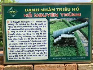 Bức ảnh chụp một bảng thông tin lịch sử đặt tại khu di tích Thành nhà Hồ, tỉnh Thanh Hóa. Bảng có nền màu xanh lá cây, viền và chữ màu vàng, được đặt trên một bức tường gạch. Nội dung trên bảng cung cấp thông tin về danh nhân Hồ Nguyên Trừng của triều đại nhà Hồ.。Toàn bộ nội dung văn bản trên bảng được ghi lại như sau:。Logo ở góc trên bên trái có chữ: 'THE HO CITADEL', 'THÀNH NHÀ HỒ', 'DI SẢN VĂN HÓA THẾ GIỚI'.。Tiêu đề lớn: 'DANH NHÂN TRIỀU HỒ HỒ NGUYÊN TRỪNG'.。Nội dung chi tiết:。'Hồ Nguyên Trừng (1374 - 1446) là con trưởng của Hồ Quý Ly. Ông là người tài năng, có nhiều phát minh mang tầm lịch sử và vươn ra khỏi biên giới quốc gia.。Ông là cha đẻ của thuyền Cổ lâu (thuyền chiến hai tầng) và ông tổ của nghề đúc súng thần công khi cải tiến loại hỏa pháo trước đó để cho ra đời khẩu “Thần cơ Thương pháo”, loại súng có uy lực mạnh nhất thời bấy giờ, góp phần tăng thêm sức mạnh cho quân sĩ nhà Hồ.。Năm 1407, giặc Minh xâm lược, ông đã bị bắt và đưa về Trung Quốc. Ông là người có công lớn trong việc chỉ huy xây Cố cung Bắc Kinh cho nhà Minh dời đô từ Nam Kinh lên Bắc Kinh.'。Bên phải bảng là hình ảnh một khẩu súng thần công cổ đặt trên bệ đá, xung quanh là bãi cỏ xanh và lối đi lát gạch. Dưới hình ảnh có chú thích: 'HỒ NGUYÊN TRỪNG - ÔNG TỔ SÚNG THẦN CÔNG'.。（日本語訳）。写真は、タインホア省の胡朝の城跡に設置された歴史案内板を写したものです。案内板は緑色の背景に金色の縁取りと文字で、レンガの壁の上に置かれています。板の内容は、胡朝時代の著名人である胡元澄（ホー・グエン・チュン）に関する情報を提供しています。板に書かれている全文は以下の通りです。左上のロゴには、「THE HO CITADEL」、「THÀNH NHÀ HỒ（胡朝の城）」、「DI SẢN VĂN HÓA THẾ GIỚI（世界文化遺産）」と書かれています。大きな見出し：「胡朝の著名人 胡元澄（ホー・グエン・チュン）」。詳細内容：。「胡元澄（ホー・グエン・チュン、1374年 - 1446年）は胡季犛（ホー・クイ・リ）の長男です。彼は才能ある人物で、歴史的な意義を持ち、国境を越える多くの発明をしました。彼は古楼船（二階建ての戦船）の生みの親であり、また、それまでの火砲を改良して当時最強の威力を持つ銃「神機銃砲」を誕生させたことで、神功砲鋳造の祖とされています。これは胡朝の兵士の戦力を増強することに貢献しました。1407年、明の侵略により、彼は捕らえられ中国に連行されました。彼は、明が南京から北京へ遷都する際の北京故宮の建設を指揮するという大きな功績を立てました。」。板の右側には、石の台座に置かれた古い神功砲の写真があり、周りには緑の芝生とレンガ敷きの通路があります。写真の下には、「胡元澄（ホー・グエン・チュン） - 神功砲の祖」というキャプションがあります。