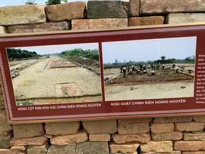 Đây là một bảng thông tin được đặt trước một bức tường xây bằng gạch cũ. Bảng thông tin có viền màu nâu đỏ, bên trên có hai bức ảnh về một cuộc khai quật khảo cổ.。Chữ viết trên bảng:。- Chú thích cho ảnh bên trái: "MÓNG CỘT ĐƠN KHU VỰC CHÍNH ĐIỆN HOÀNG NGUYÊN".。- Chú thích cho ảnh bên phải: "KHAI QUẬT CHÍNH ĐIỆN HOÀNG NGUYÊN".。- Ở phía bên phải của bảng có một đoạn văn bản mô tả nhưng bị cắt mất một phần, chỉ đọc được một vài từ như: "Khai", "điện", "móng", "Hệ th", "nhuộm", "trên đ", "đã mi", "Đối v", "trọng", "đó. Ch", "thủy, C", "là Thiê", "thông c".。Mô tả cảnh vật và hoạt động:。- Loại địa điểm: Một địa điểm khai quật khảo cổ hoặc khu trưng bày di tích lịch sử.。- Hoạt động cụ thể: Bức ảnh bên phải cho thấy một nhóm người, nhiều người trong số họ đội nón lá, đang tiến hành khai quật khảo cổ trên một khu đất rộng. Họ đang đào đất và làm việc tại hiện trường. Bức ảnh bên trái cho thấy kết quả của việc khai quật, đó là phần nền móng của một công trình kiến trúc cổ.。- Các vật thể được chụp: Bảng thông tin, các bức ảnh về công trường khai quật, nền móng kiến trúc, các nhà khảo cổ/công nhân, nón lá, và một bức tường gạch cổ ở hậu cảnh.。（日本語訳）。これは、古いレンガで造られた壁の前に設置された案内板です。案内板は赤褐色の縁取りがあり、上部には考古学的な発掘調査に関する写真が2枚あります。案内板の文字：。- 左の写真のキャプション：「ホアン・グエン正殿区域の単柱の基礎」。- 右の写真のキャプション：「ホアン・グエン正殿の発掘」。- 案内板の右側には説明文の一節がありますが、一部が途切れており、「Khai」、「điện」、「móng」、「Hệ th」、「nhuộm」、「trên đ」、「đã mi」、「Đối v」、「trọng」、「đó. Ch」、「thủy, C」、「là Thiê」、「thông c」といったいくつかの単語しか読み取れません。風景と活動の説明：。- 場所の種類：考古学的な発掘現場、または歴史的遺跡の展示エリア。- 具体的な活動：右の写真は、その多くがノンラー（菅笠）をかぶった一団の人々が、広大な土地で考古学的な発掘を行っている様子を示しています。彼らは土を掘り、現場で作業しています。左の写真は発掘の結果を示しており、それは古代の建築物の基礎部分です。- 撮影されている物：案内板、発掘現場の写真、建築物の基礎、考古学者/作業員、ノンラー（菅笠）、そして背景にある古いレンガの壁。