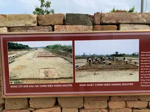 Đây là hình ảnh một bảng thông tin đặt trước một bức tường gạch cổ. Bảng thông tin có nền màu đỏ sẫm, chữ trắng, viền hoa văn, cung cấp thông tin về một cuộc khai quật khảo cổ.。Nội dung văn bản trên bảng:。- Chú thích ảnh bên trái: "MÓNG CỘT ĐƠN KHU VỰC CHÍNH ĐIỆN HOÀNG NGUYÊN"。- Chú thích ảnh bên phải: "KHAI QUẬT CHÍNH ĐIỆN HOÀNG NGUYÊN"。- Đoạn văn bản bên phải bị che một phần, các từ có thể đọc được là: "Khai quật điện được... móng cột... Hệ thống... nhuộm m... trên được... đã minh c... Đối với kh... trọng nhất... đó. Chính... thủy, Chính... là Thiên tu... thông qua..."。Miêu tả cảnh vật và hoạt động:。- Địa điểm: Một khu di tích khảo cổ, cụ thể là khu vực khai quật Chính Điện Hoàng Nguyên. Bảng thông tin được đặt ngoài trời, phía trước một bức tường gạch cũ.。- Hoạt động: Bảng thông tin mô tả hoạt động khai quật khảo cổ. Bức ảnh bên phải cho thấy một nhóm người (có thể là các nhà khảo cổ học hoặc công nhân) đang tiến hành khai quật. Nhiều người trong số họ đội nón lá để che nắng.。- Vật thể trong ảnh: Bảng thông tin, tường gạch cổ, công trường khai quật, nền móng kiến trúc cổ, con người, nón lá, và các dụng cụ khai quật như xô và xe cút kít.。（日本語訳）。これは、古いレンガの壁の前に置かれた案内板の画像です。案内板は、暗い赤色の背景に白い文字、花模様の縁取りがあり、ある考古学的な発掘調査に関する情報を提供しています。案内板のテキスト内容：。- 左側の写真のキャプション：「ホアン・グエン正殿地区の単一柱の基礎」。- 右側の写真のキャプション：「ホアン・グエン正殿の発掘」。- 右側の文章は一部が隠れており、読み取れる単語は次の通りです：「殿の発掘は...柱の基礎...システム...染め...上は...証明した...にとって...最も重要...それ。まさに...水、まさに...天修...通じて...」。風景と活動の描写：。- 場所：ある考古学遺跡、具体的にはホアン・グエン正殿の発掘エリア。案内板は屋外に、古いレンガの壁の前に設置されています。- 活動：案内板は考古学的な発掘活動について説明しています。右側の写真は、一団の人々（考古学者または作業員の可能性があります）が発掘作業を行っている様子を示しています。彼らの多くは日差しを避けるためにノンラーをかぶっています。- 写真の中の物体：案内板、古いレンガの壁、発掘現場、古代建築の基礎、人々、ノンラー、そしてバケツや手押し車などの発掘道具。