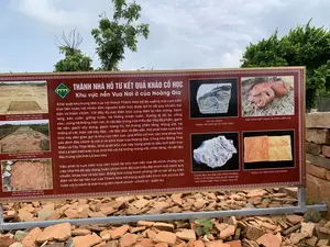 Bức ảnh chụp một bảng thông tin lớn được đặt ngoài trời tại một khu di tích khảo cổ. Phía trước và bên dưới bảng là một đống các mảnh gạch, ngói vỡ cũ. Phía sau là cây cối và bầu trời. Bảng thông tin này mô tả về các kết quả khảo cổ học tại Thành Nhà Hồ.。**Nội dung được ghi trên bảng:**。**Tiêu đề:**。THÀNH NHÀ HỒ TỪ KẾT QUẢ KHẢO CỔ HỌC。Khu vực nền Vua Nơi ở của Hoàng Gia。**Nội dung chính:**。Khai quật khu trung tâm của nội thành Thành Nhà Hồ đã xuất lộ một cụm kiến trúc liên hoàn với nhiều đơn nguyên kiến trúc được bố trí rất quy chuẩn, bài bản và hoàn chỉnh. Với đầy đủ các kiến trúc cung điện từ nền móng, hành lang, sân vườn, giếng nước, hệ thống thoát nước, đường đi lối lại, cổng vào...cùng hệ thống hiện vật, di vật đặc trưng của triều đại như đá phiến, gạch lát nền, gạch xây dựng, gạch trang trí, hệ thống chân tảng, móng cột, hệ thống di vật, hiện vật dày đặc...rất độc đáo và đặc sắc. Nơi phát hiện cụm kiến trúc này dân gian gọi là khu vực nền vua, qua khảo cổ học các nhà khoa học xác định đây chính là nơi ở và sinh hoạt của Hoàng Gia. Cũng như Đông Thái Miếu và Tây Thái Miếu, khai quật khu vực này cũng phát lộ dấu tích kiến trúc thời Lê bên trên kiến trúc thời Hồ với hệ thống móng cột, chân tảng, và vật liệu đặc trưng của thời Lê sau này.。Việc phát lộ cụm kiến trúc liên hoàn tại khu vực nền vua đã minh chứng cho việc nhà Hồ đã xây dựng hoàn chỉnh kinh đô của triều đại mình một cách quy chuẩn, khoa học và bài bản. Đồng thời cũng minh chứng rất rõ nét về sự hiện diện và tồn tại liên tục của Thành Nhà Hồ trong suốt tiến trình lịch sử của đất nước với tư cách là một trung tâm hành chính - chính trị - quân sự.。**Chú thích hình ảnh trên bảng:**。- DẤU TÍCH MÓNG CỘT KIẾN TRÚC CHÍNH 17 GIAN KHU VỰC TRUNG TÂM NỀN VUA。- NỀN SÂN GẠCH VUÔNG DIỆN TÍCH LỚN TRUNG TÂM NỀN VUA。- DẤU TÍCH DẢI ĐƯỜNG HOA CHANH PHÍA ĐÔNG NAM KHU VỰC NỀN VUA。- ĐÁ XÂY DỰNG TRANG TRÍ HÌNH SƯ TỬ THỜI TRẦN。- ĐẦU RỒNG ĐẤT NUNG TẠI ĐÔNG NỀN VUA。- THÀNH BẬC ĐÁ HOA VĂN CHIM PHƯỢNG THỜI LÝ Ở THĂNG LONG ĐƯỢC DÙNG ĐỂ XÂY DỰNG KIẾN TRÚC THÀNH NHÀ HỒ。- GẠCH LÁT NỀN HÌNH HOA CHANH。**Mô tả cảnh vật và hoạt động:**。- **Loại địa điểm:** Khu di tích khảo cổ (Thành Nhà Hồ).。- **Hoạt động:** Không có hoạt động của con người. Bức ảnh chụp một bảng thông tin tĩnh để cung cấp kiến thức cho khách tham quan.。- **Vật thể trong ảnh:** Bảng thông tin, các mảnh vỡ của gạch và ngói cổ, cây cối.。（日本語訳）。写真は、考古学遺跡の屋外に設置された大きな案内板を写したものです。板の前と下には、古いレンガや瓦の破片の山があります。後ろには木々と空が見えます。この案内板は、胡朝の城（タイン・ニャー・ホー）における考古学的成果について説明しています。**ボードに記載されている内容：**。**タイトル：**。考古学的成果から見た胡朝の城。王の基壇地区 王家の居住地。**主な内容：**。胡朝の城の内城中心部を発掘したところ、非常に規格正しく、体系的かつ完全に配置された、多くの建築単位からなる一連の建築群が露わになりました。基礎、廊下、庭園、井戸、排水システム、通路、門などの宮殿建築が完全に揃っており、粘板岩、床敷きレンガ、建築用レンガ、装飾レンガ、礎盤システム、柱の基礎、密集した遺物・遺構システムなど、王朝特有の非常にユニークで特色ある遺物・遺構システムも伴っています。この建築群が発見された場所は、民間では「王の基壇地区」と呼ばれており、考古学を通じて科学者たちはここがまさに王家の居住および生活の場であったと特定しました。東太廟および西太廟と同様に、この地区の発掘では、胡朝時代の建築の上に、後の黎朝時代の特徴的な柱の基礎、礎盤、および建材のシステムを持つ黎朝時代の建築の痕跡も発見されました。王の基壇地区で一連の建築群が発見されたことは、胡朝が自らの王朝の首都を規格正しく、科学的かつ体系的に完全に建設したことを証明しました。同時に、行政・政治・軍事の中心地として、国の歴史の全過程を通じて胡朝の城が継続的に存在し続けたことをも非常にはっきりと証明しています。**ボード上の写真のキャプション：**。- 王の基壇地区中心部にある17間の主要建築の柱の基礎の痕跡。- 王の基壇地区中心部にある広大な正方形のレンガ敷きの中庭の床。- 王の基壇地区南東部のチャンパの花模様の道の痕跡。- 陳朝時代の獅子形の装飾建築石。- 王の基壇東部にあるテラコッタ製の龍の頭。- 昇龍（タンロン）にあった李朝時代の鳳凰文様の石の階段の欄干で、胡朝の城の建築に使用されたもの。- チャンパの花模様の床敷きレンガ。**風景と活動の説明：**。- **場所の種類：** 考古学遺跡（胡朝の城）。- **活動：** 人間の活動はない。写真は、来訪者に見識を提供するための静的な案内板を写したものである。- **写真の中の物体：** 案内板、古いレンガや瓦の破片、木々。