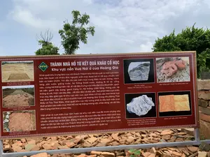 Bức ảnh chụp một bảng thông tin lớn đặt ngoài trời tại một khu di tích khảo cổ, cụ thể là Thành Nhà Hồ. Phía sau bảng là cây xanh và bầu trời. Bên dưới bảng là các mảnh vỡ của gạch, ngói và đá, là những hiện vật khảo cổ được trưng bày. Bảng thông tin có nền màu nâu đỏ, chữ màu trắng và vàng, cung cấp thông tin chi tiết về kết quả khai quật khảo cổ tại đây.。Nội dung văn bản trên bảng như sau:。Tiêu đề lớn: THÀNH NHÀ HỒ TỪ KẾT QUẢ KHẢO CỔ HỌC。Tiêu đề phụ: Khu vực nền Vua Nơi ở của Hoàng Gia。Đoạn văn chính:。Khai quật khu trung tâm của nội thành Thành Nhà Hồ đã xuất lộ một cụm kiến trúc liên hoàn với nhiều đơn nguyên kiến trúc được bố trí rất quy chuẩn, bài bản và hoàn chỉnh. Với đầy đủ các kiến trúc cung điện từ nền móng, hành lang, sân vườn, giếng nước, hệ thống thoát nước, đường đi lối lại, cổng vào...cùng hệ thống hiện vật, di vật đặc trưng của triều đại như đá phiến, gạch lát nền, gạch xây dựng, gạch trang trí, hệ thống chân tảng, móng cột, hệ thống di vật, hiện vật dày đặc...rất độc đáo và đặc sắc. Nơi phát hiện cụm kiến trúc này dân gian gọi là khu vực nền vua, qua khảo cổ học các nhà khoa học xác định đây chính là nơi ở và sinh hoạt của Hoàng Gia. Cũng như Đông Thái Miếu và Tây Thái Miếu, khai quật khu vực này cũng phát lộ dấu tích kiến trúc thời Lê bên trên kiến trúc thời Hồ với hệ thống móng cột, chân tảng, và vật liệu đặc trưng của thời Lê sau này.。Việc phát lộ cụm kiến trúc liên hoàn tại khu vực nền vua đã minh chứng cho việc nhà Hồ đã xây dựng hoàn chỉnh kinh đô của triều đại mình một cách quy chuẩn, khoa học và bài bản. Đồng thời cũng minh chứng rất rõ nét về sự hiện diện và tồn tại liên tục của Thành Nhà Hồ trong suốt tiến trình lịch sử của đất nước với tư cách là một trung tâm hành chính - chính trị - quân sự.。Chú thích cho các hình ảnh trên bảng:。- DẤU TÍCH MÓNG CỘT KIẾN TRÚC CHÍNH 17 GIAN KHU VỰC TRUNG TÂM NỀN VUA。- NỀN SÂN GẠCH VUÔNG DIỆN TÍCH LỚN TRUNG TÂM NỀN VUA。- DẤU TÍCH DẢI ĐƯỜNG HOA CHANH PHÍA ĐÔNG NAM KHU VỰC NỀN VUA。- ĐÁ XÂY DỰNG TRANG TRÍ HÌNH SƯ TỬ THỜI TRẦN。- ĐẦU RỒNG ĐẤT NUNG TẠI ĐỒNG NỀN VUA。- THÀNH BẬC ĐÁ HOA VĂN CHIM PHƯỢNG THỜI LÝ Ở THĂNG LONG ĐƯỢC DÙNG ĐỂ XÂY DỰNG KIẾN TRÚC THÀNH NHÀ HỒ。- GẠCH LÁT NỀN HÌNH HOA CHANH。（日本語訳）。写真は、考古学遺跡、具体的には胡朝の城塞に屋外に設置された大きな案内板を写したものです。案内板の後ろには緑の木々と空が見えます。案内板の下には、展示されている考古学的遺物であるレンガ、瓦、石の破片があります。案内板は赤茶色の背景に白と黄色の文字で、ここでの考古学発掘調査の結果に関する詳細な情報を提供しています。案内板の文章内容は以下の通りです。大見出し：考古学的成果から見た胡朝の城塞。副見出し：王の基壇地区 王家の居住地。本文：。胡朝の城塞の内城中心部の発掘調査により、多くの建築単位が非常に規格正しく、体系的かつ完全に配置された一連の建築群が明らかになりました。基礎、廊下、庭園、井戸、排水システム、通路、門などの宮殿建築が完全に揃っており、粘板岩、床タイル、建築用レンガ、装飾レンガ、礎石システム、柱の基礎、密集した遺物・遺品システムなど、王朝特有の遺物・遺品群と共に、非常にユニークで特色があります。この建築群が発見された場所は、民間では「王の基壇地区」と呼ばれており、考古学を通じて科学者たちはここが王家の居住および生活の場であったと特定しました。東太廟と西太廟と同様に、この地区の発掘調査では、胡朝時代の建築の上に、後の黎朝時代の特徴的な柱の基礎、礎石、および建材のシステムを持つ黎朝時代の建築の痕跡も発見されました。王の基壇地区で一連の建築群が発見されたことは、胡朝が自らの王朝の首都を規格正しく、科学的かつ体系的に完全に建設したことを証明しています。同時に、国の歴史の全過程を通じて、行政・政治・軍事の中心地として胡朝の城塞が継続的に存在し続けたことを非常にはっきりと証明しています。案内板上の写真のキャプション：。- 王の基壇地区中心部の17間の主建築の柱の基礎の痕跡。- 王の基壇地区中心部の広大な正方形レンガ敷きの中庭の床。- 王の基壇地区南東部のホアチャン（レモンの花）模様の道の痕跡。- 陳朝時代のライオン形の装飾建築石。- 王の基壇地区のテラコッタ製龍頭。- 胡朝の城塞の建築に使用された、タンロン（昇龍）の李朝時代の鳳凰文様の石の階段の欄干。- ホアチャン（レモンの花）模様の床タイル