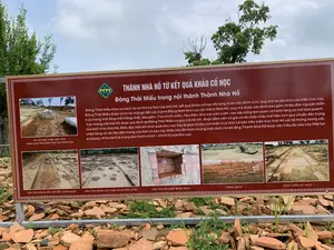 Bức ảnh chụp một tấm bảng thông tin lớn đặt ngoài trời tại một khu di tích khảo cổ, cụ thể là Thành Nhà Hồ. Tấm bảng có nền màu nâu, chữ màu trắng, được đặt trên một giá đỡ kim loại. Phía dưới và xung quanh chân bảng là nền đất phủ đầy các mảnh gạch ngói cũ vỡ, xen lẫn một ít cỏ dại. Phía sau là cây cối xanh tươi và bầu trời. Tấm bảng này cung cấp thông tin chi tiết về các kết quả khảo cổ học tại Đông Thái Miếu.。Nội dung văn bản được ghi trên bảng như sau:。**Tiêu đề lớn:**。THÀNH NHÀ HỒ TỪ KẾT QUẢ KHẢO CỔ HỌC。Đông Thái Miếu trong nội thành Thành Nhà Hồ。**Nội dung chi tiết:**。Đông Thái miếu theo sử sách là nơi thờ họ Nội của nhà Hồ, kết quả Khảo cổ học đã từng bước xác định vị trí, quy mô và cấu trúc của kiến trúc này. Đông Thái Miếu được bố trí tại một gò đất cao ở phía Đông Nam khu vực nội thành Nhà Hồ; quy mô được xác định bao gồm nhiều đơn nguyên kiến trúc trong một tổng thể thống nhất, bao gồm: Tòa chính miếu, hậu điện, khu vực sân vườn, các lớp cổng tam quan và hành lang có mái bao quanh. Các móng cột thời Hồ được xác định tại Đông Thái Miếu có quy mô rất lớn, được đầm nền và gia cố rất chắc chắc thể hiện tính quy chuẩn đặc trưng của kiến trúc thời Hồ. Điều đặc biệt khi khai quật khu vực này là phát lộ dấu tích kiến trúc thời Lê bên trên kiến trúc thời Hồ với hệ thống móng cột, chân tảng và vật liệu đặc trưng của thời Lê sau này. Điều này đã minh chứng một cách rõ nét rằng Thành Nhà Hồ được các triều đại sau này tiếp tục sử dụng với tư cách là trung tâm hành chính - chính trị của khu vực.。**Các hình ảnh và chú thích kèm theo:**。Tấm bảng có các hình ảnh chụp lại các di tích đã được khai quật, với các chú thích tương ứng:。- CHI TIẾT BẬC THỀM KIẾN TRÚC HÀNH LANG PHÍA ĐÔNG KHU VỰC ĐÔNG NAM。- DẤU TÍCH MÓNG NỀN, BÓ NỀN, CỐNG NƯỚC。- DẤU TÍCH MÓNG CỘT THỜI HỒ VÀ THỜI LÊ SƠ。- DẤU TÍCH BỂ NƯỚC BẰNG GẠCH。- TƯỜNG GẠCH。- HÀNH LANG LÁT GẠCH。（日本語訳）。写真は、考古学遺跡、具体的には胡朝の城塞に屋外設置された大きな案内板を写したものです。案内板は茶色の背景に白文字で、金属製の支柱に設置されています。案内板の下とその脚の周りは、古い割れたレンガや瓦の破片で覆われた地面で、雑草が少し混じっています。後ろには青々とした木々と空が見えます。この案内板は、東太廟における考古学的成果に関する詳細な情報を提供しています。案内板に記載されている文章の内容は以下の通りです。**大きな見出し:**。考古学的成果から見た胡朝の城塞。胡朝の城塞内城にある東太廟。**詳細内容:**。史書によると、東太廟は胡朝の内戚を祀る場所であり、考古学的成果によってこの建築物の位置、規模、構造が段階的に特定されました。東太廟は、胡朝の城塞内城地区の南東にある高台に配置されています。その規模は、本廟、後殿、庭園エリア、複数の三関門、そして周囲を囲む屋根付きの回廊を含む、統一された全体像の中に多くの建築単位が含まれていると特定されています。東太廟で確認された胡朝時代の柱の基礎は非常に大規模で、地盤が固められ、非常に強固に補強されており、胡朝時代の建築に特有の規格性を示しています。この地域の発掘で特筆すべきは、胡朝時代の建築物の上に、後の黎朝時代の柱の基礎、礎石、そして特有の建材のシステムを持つ黎朝時代の建築遺跡が発見されたことです。このことは、胡朝の城塞が後の王朝によって地域の行政・政治の中心として継続的に使用されていたことを明確に証明しています。**付随する写真とキャプション:**。案内板には、発掘された遺跡を撮影した写真が、それぞれのキャプションと共に掲載されています。- 南東地区東側回廊建築の階段の詳細。- 基礎、基礎の縁、排水溝の痕跡。- 胡朝時代と黎初時代の柱の基礎の痕跡。- レンガ造りの貯水槽の痕跡。- レンガの壁。- レンガ敷きの回廊