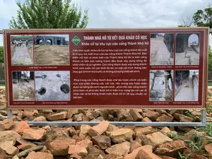 Bức ảnh chụp một tấm biển thông tin lớn đặt ngoài trời tại khu di tích lịch sử Thành Nhà Hồ. Tấm biển có nền màu nâu, chữ màu trắng và vàng, được đặt trên một đống đá và gạch vỡ. Phía sau tấm biển là cây cối xanh tươi và bầu trời u ám.。Nội dung văn bản trên biển được ghi lại đầy đủ như sau:。Tiêu đề chính: THÀNH NHÀ HỒ TỪ KẾT QUẢ KHẢO CỔ HỌC。Tiêu đề phụ: Khảo cổ tại khu vực các cổng Thành Nhà Hồ。Nội dung chi tiết:。"Việc khai quật, khảo cổ học tại khu vực các cổng thành đã xuất lộ rõ quy mô, kiến trúc của các cổng thành Thành Nhà Hồ. Đặc điểm nổi bật và khác biệt của Thành Nhà Hồ đó là bốn cổng thành và bốn bức tường thành đều được xây dựng bằng đá chắc chắn và uy nghiêm. Các cổng thành được xây dựng thành hình vòm cuốn với các khối đá lớn có mặt cắt hình thang cân (hay gọi là hình múi bưởi) và không sử dụng chất kết dính.。Phía trong các cổng thành được chế tác hoàn chỉnh với kiến trúc của phần khung cửa, cối cửa, nền móng cửa hoàn toàn được lát bằng đá xanh nguyên khối...phía trên các cổng thành phía Nam và phía bắc được bố trí kiến trúc vọng lâu với các lỗ chân cột và hệ thống thoát nước được bố trí rất quy chuẩn và bài bản."。Trên biển còn có các hình ảnh minh họa kèm chú thích:。- Ảnh các nhà khảo cổ đang làm việc và ảnh cổng thành bằng đá với chú thích: "KHAI QUẬT TẠI VỊ TRÍ CỔNG NAM"。- Ảnh hàng đá kè móng tường với chú thích: "HÀNG KÈ ĐÁ MÓNG TƯỜNG"。- Ảnh lối đi bên trong cổng thành với chú thích: "KHAI QUẬT TẠI VỊ TRÍ CỔNG ĐÔNG"。- Ảnh một khối đá có lỗ tròn (cối cửa) với chú thích: "DẤU TÍCH CỐI CỬA"。- Ảnh lối đi lát đá dọc theo tường thành với chú thích: "KHAI QUẬT TẠI VỊ TRÍ CỔNG TÂY"。- Ảnh các lỗ trên nền đá với chú thích: "DẤU TÍCH VỌNG LÂU TRÊN CỔNG BẮC"。- Ảnh lối đi được khai quật với chú thích: "KHAI QUẬT TẠI VỊ TRÍ CỔNG BẮC"。Hoạt động được mô tả là công tác khai quật và nghiên cứu khảo cổ học tại di tích Thành Nhà Hồ.。（日本語訳）。写真は、胡朝の城跡歴史地区に屋外設置された大きな案内板を写したものです。案内板は茶色の背景に白と黄色の文字で、石と割れたレンガの山の上に置かれています。案内板の後ろには青々とした木々と曇り空が広がっています。案内板の文面は以下の通りです。主見出し：考古学の成果から見た胡朝の城。副見出し：胡朝の城の各城門区域における考古学調査。詳細内容：。「城門区域における発掘・考古学調査により、胡朝の城の各城門の規模と建築様式が明らかになりました。胡朝の城の際立った特徴は、4つの城門と4つの城壁がすべて頑丈で荘厳な石で造られていることです。各城門は、断面が等脚台形（またはザボンの房の形と呼ばれる）の大きな石塊を用いたアーチ型に組まれ、接着剤は使用されていません。各城門の内側は、扉の枠、扉の軸受け、扉の基礎が完全に青石の一枚岩で敷き詰められるなど、完璧な建築様式で造られています...南門と北門の上部には、柱の穴と排水システムが非常に規格化され、体系的に配置された望楼建築が設けられています。」。案内板には、キャプション付きの図解写真もあります。- 作業中の考古学者と石造りの城門の写真、キャプション：「南門跡での発掘」。- 城壁の基礎を固める石積みの写真、キャプション：「城壁基礎の石積み」。- 城門内部の通路の写真、キャプション：「東門跡での発掘」。- 丸い穴のある石塊（扉の軸受け）の写真、キャプション：「扉の軸受けの痕跡」。- 城壁に沿った石畳の通路の写真、キャプション：「西門跡での発掘」。- 石の基礎にある複数の穴の写真、キャプション：「北門上の望楼の痕跡」。- 発掘された通路の写真、キャプション：「北門跡での発掘」。記述されている活動は、胡朝の城跡における発掘および考古学研究作業です。